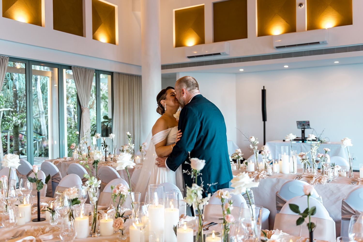 Couple shares a tender kiss on the dance floor surrounded by white candles and floral wedding decor.