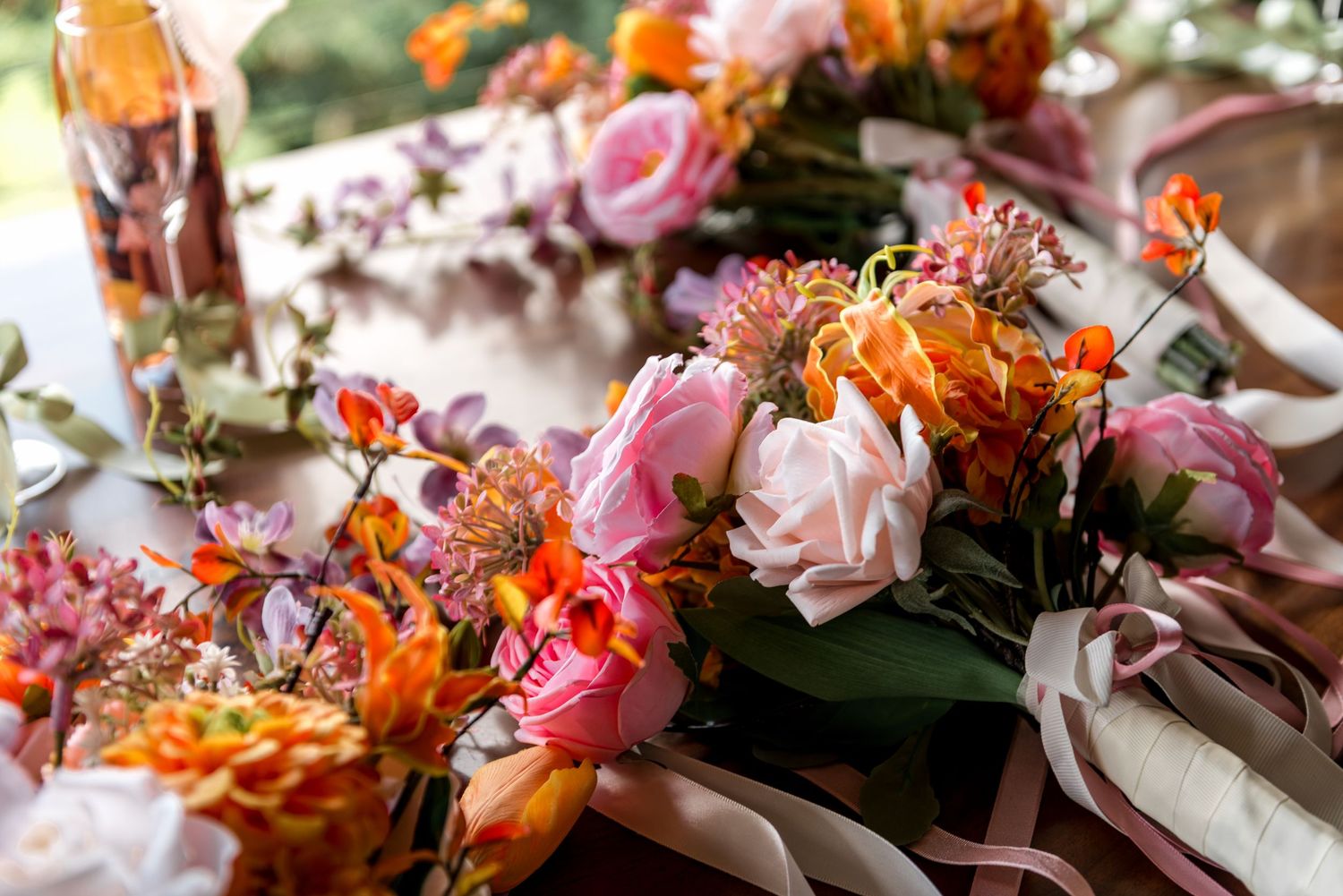 Vibrant pink and orange wedding floral arrangement with roses and wildflowers on a reception table.