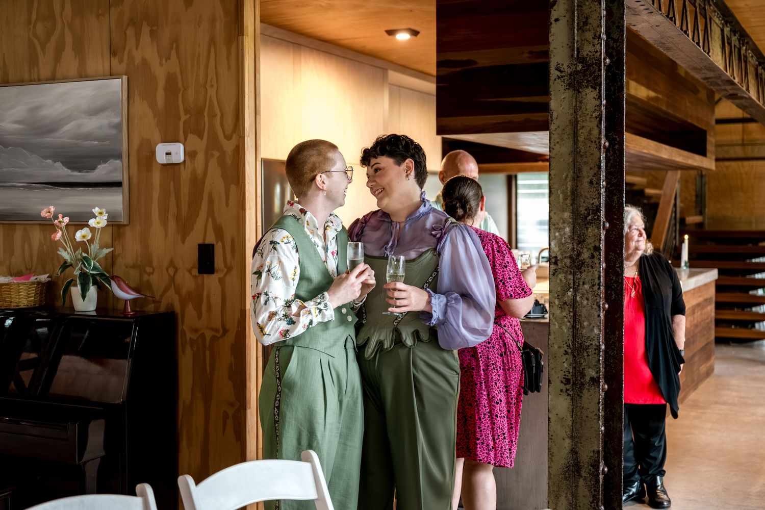 Two smiling wedding guests in green outfits chatting inside a wooden venue.