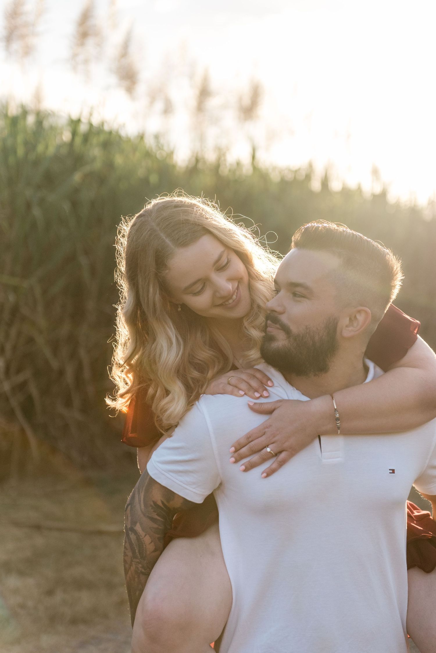A smiling woman hugs a bearded man giving her a piggyback ride at golden hour.