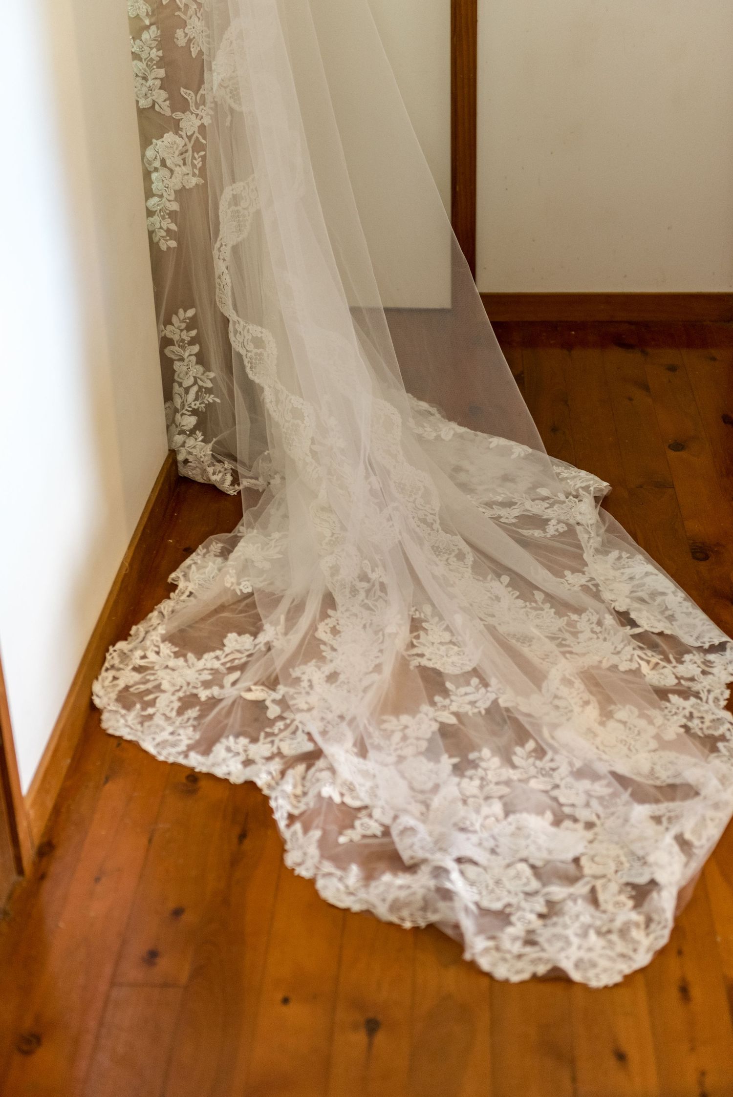 Elegant lace cathedral wedding veil with floral embroidery trailing on a wooden floor.