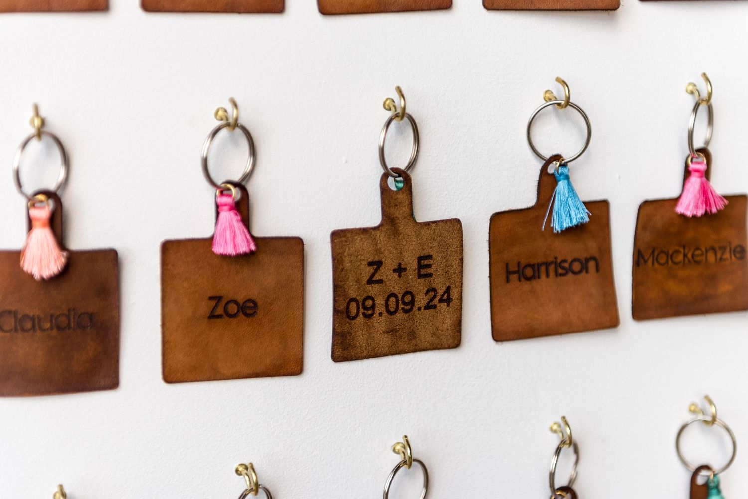 Personalized laser engraved leather keyrings with colorful tassels and guest names on white display board.