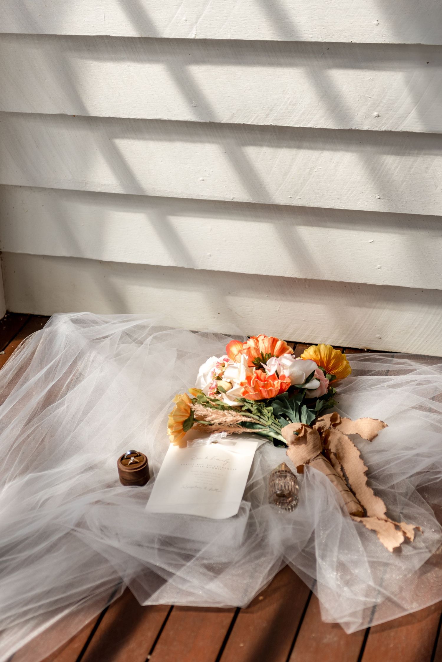 Bridal bouquet with orange and white flowers resting on tulle wedding dress outdoors.