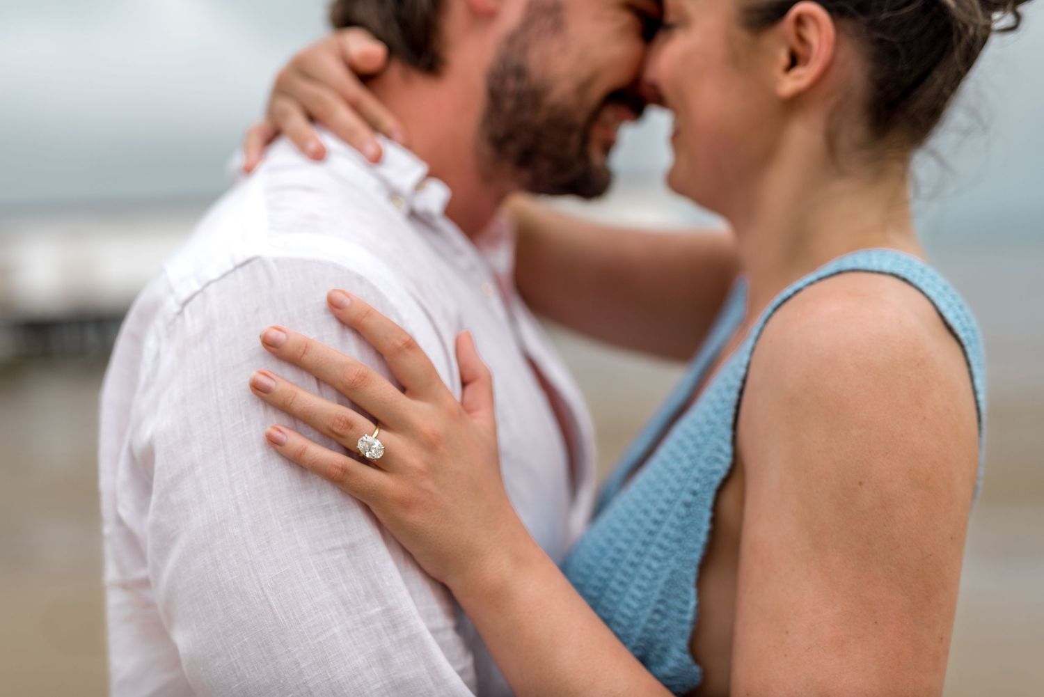 Close-up of an engaged couple nearly kissing with focus on a sparkling diamond engagement ring on her hand.