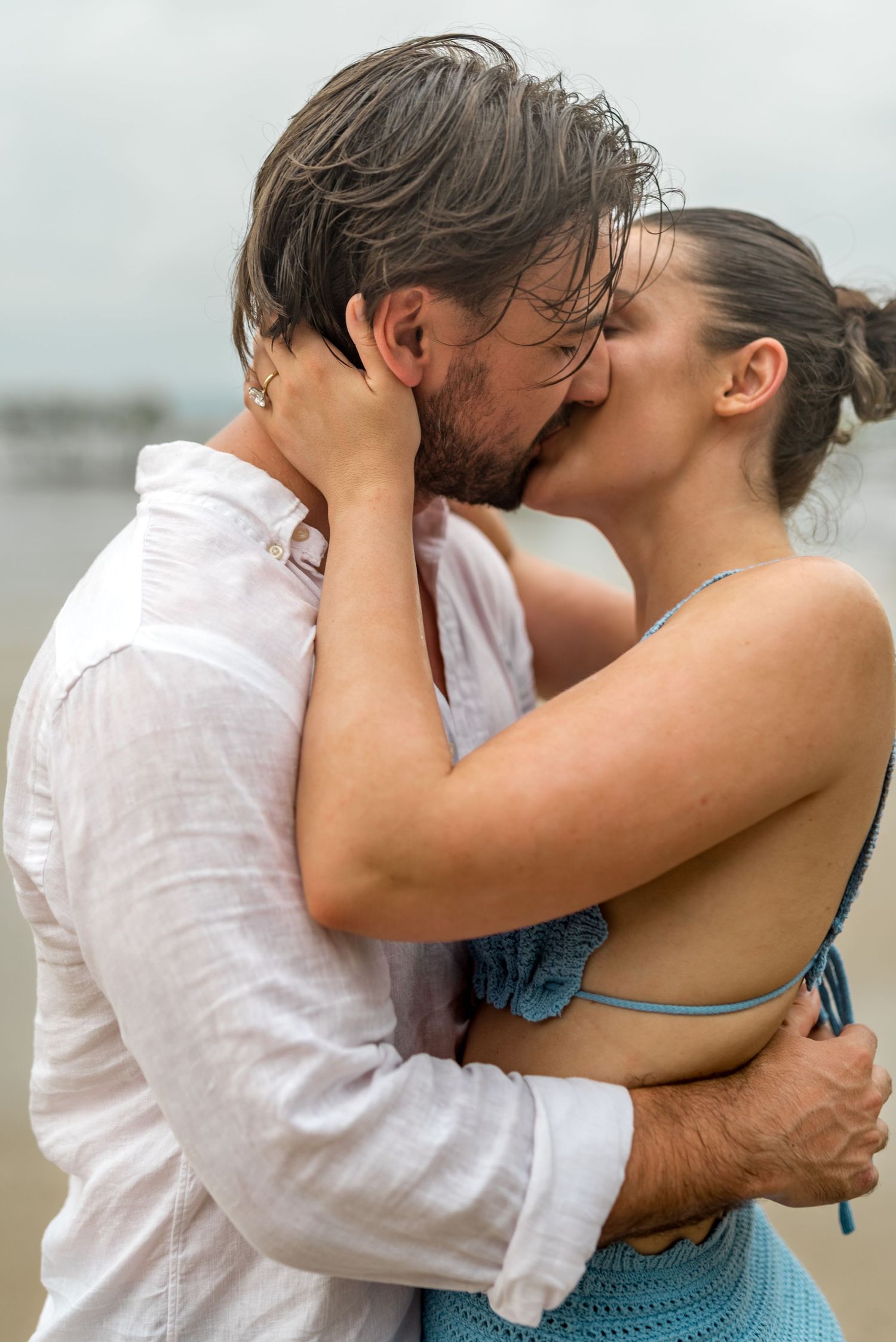 Passionate couple kissing in the rain on a beach, both with wet hair and embracing closely.