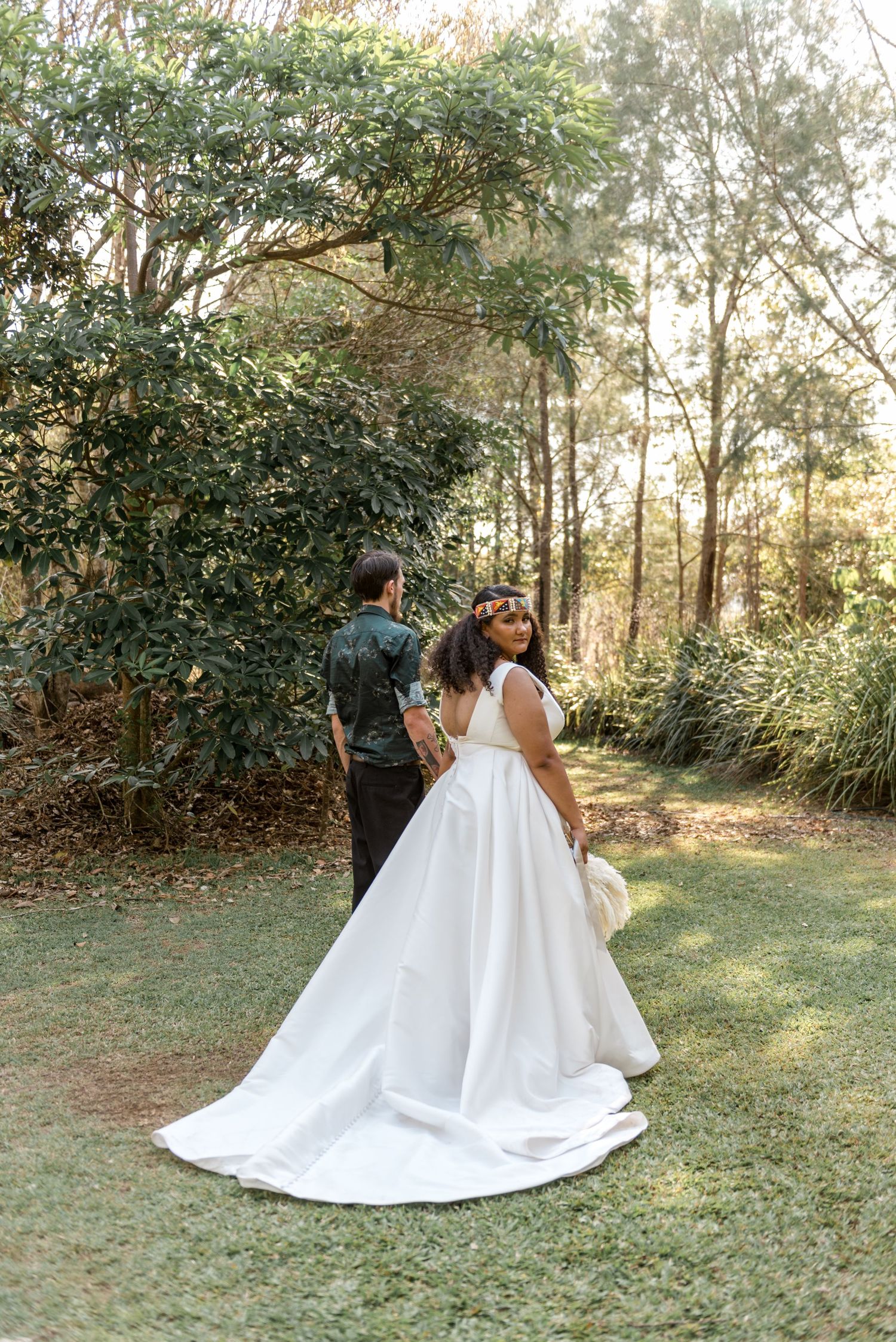 Bride in elegant white gown with long train walking with groom through a scenic garden.