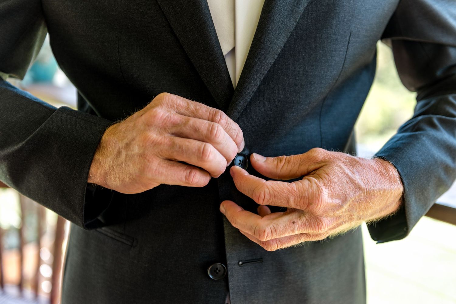 Groom in a dark suit buttoning his jacket lapel while getting ready for his wedding.