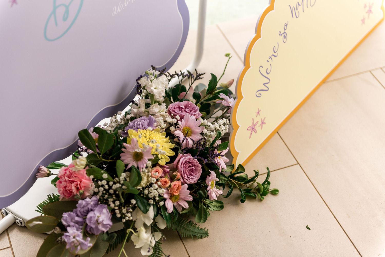 Close-up of vibrant mixed floral wedding bouquet with pink carnations and purple blooms on tile floor.