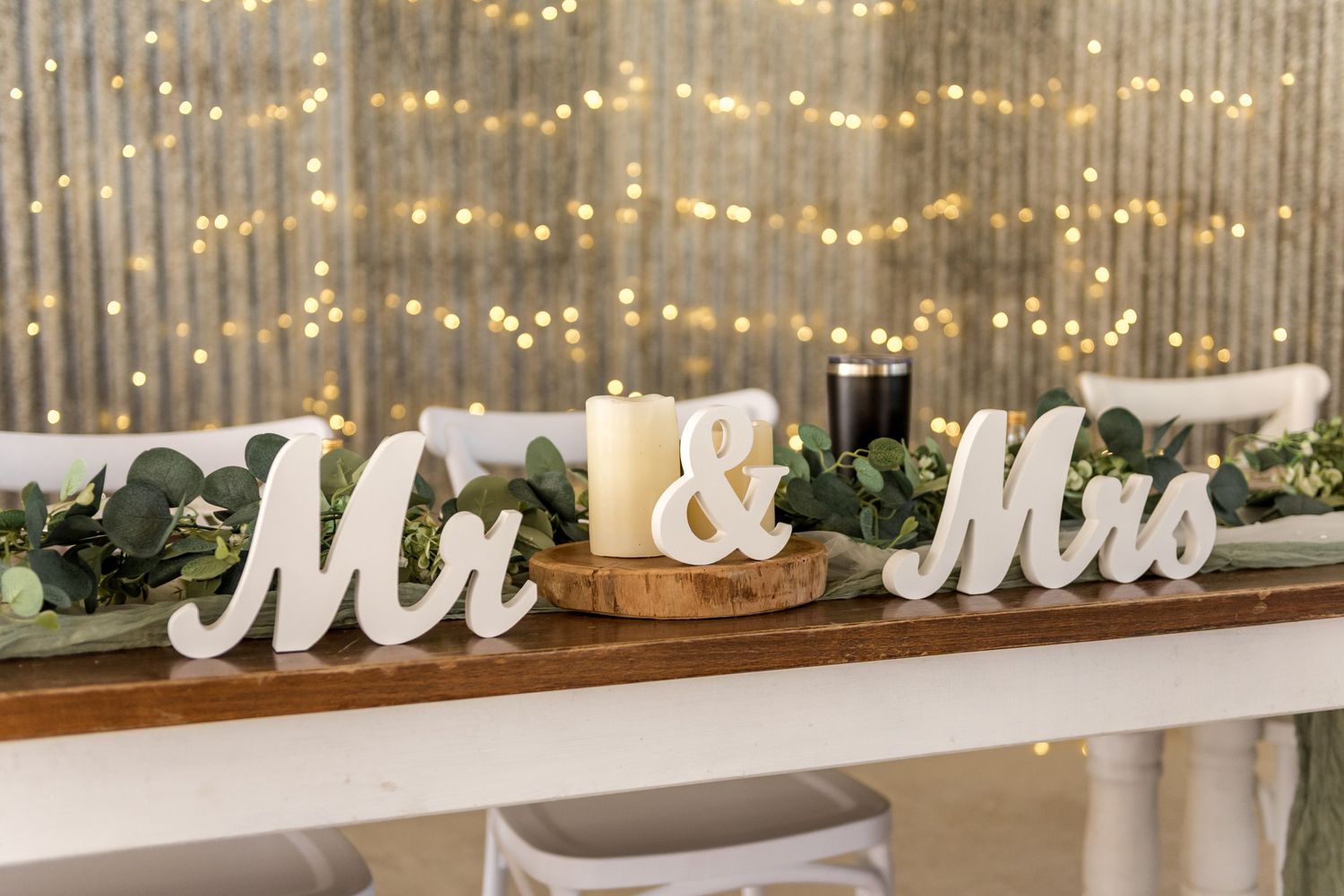 Elegant Mr and Mrs wooden signs with candles and greenery on wedding reception table.