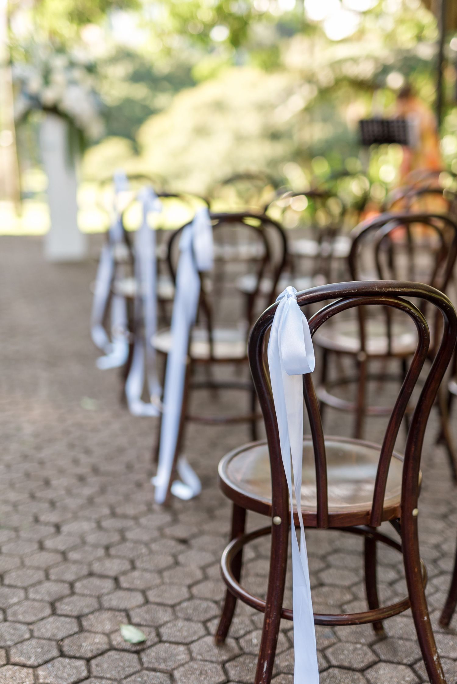 Elegant dark wooden Thonet chairs with white ribbon bows arranged for an outdoor garden wedding ceremony.