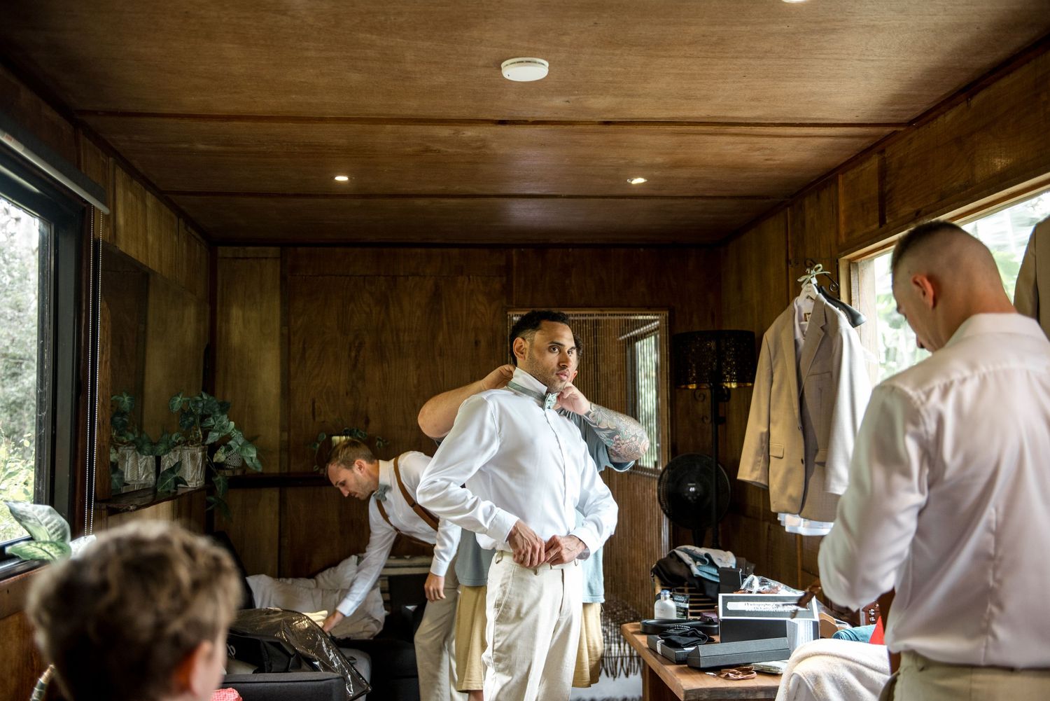 Groomsmen getting dressed in a rustic wooden cabin room preparing for a wedding ceremony.