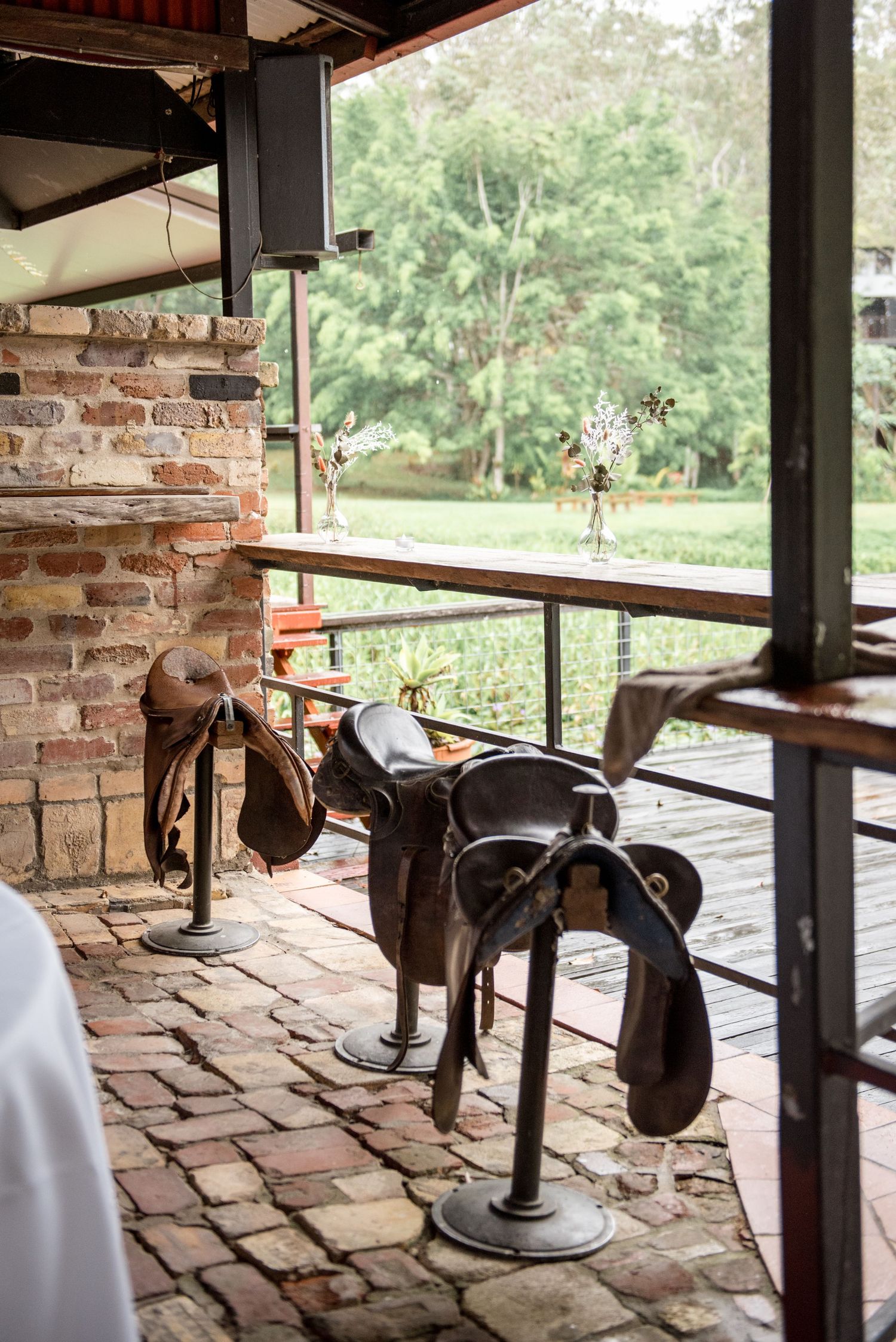 Vintage leather horse saddles displayed on stands inside a rustic brick wedding venue.