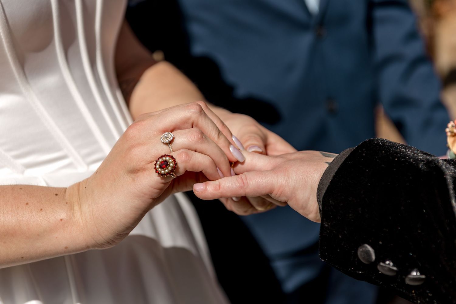 Close-up of bride placing a gold ring on groom's finger during outdoor wedding ceremony.