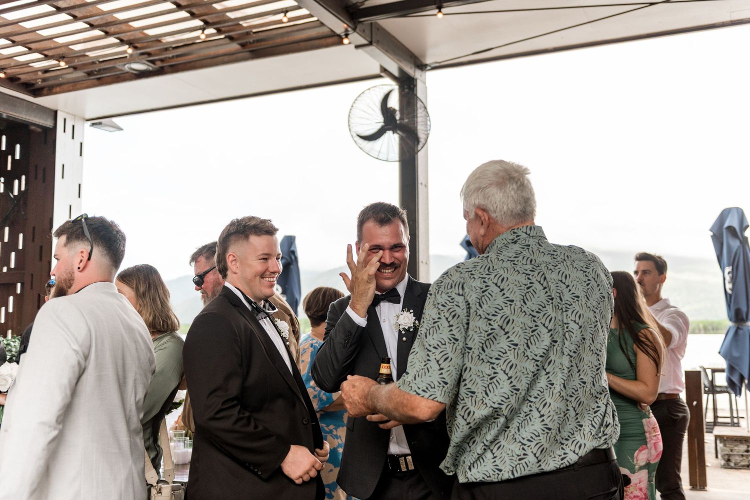 Guests laughing and socializing at an outdoor wedding reception under a pergola.