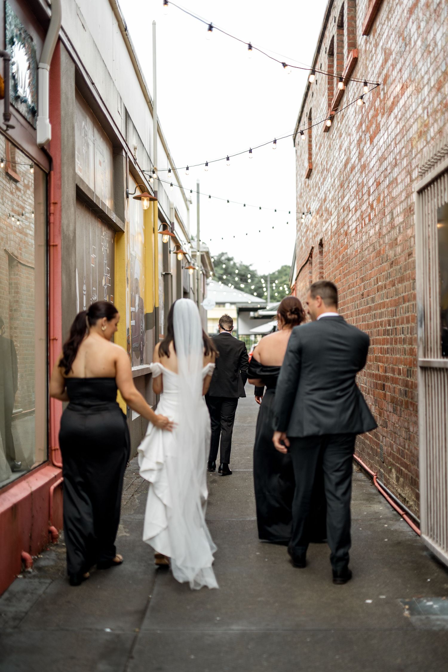 Bride in white gown and bridal party walking through a charming laneway.