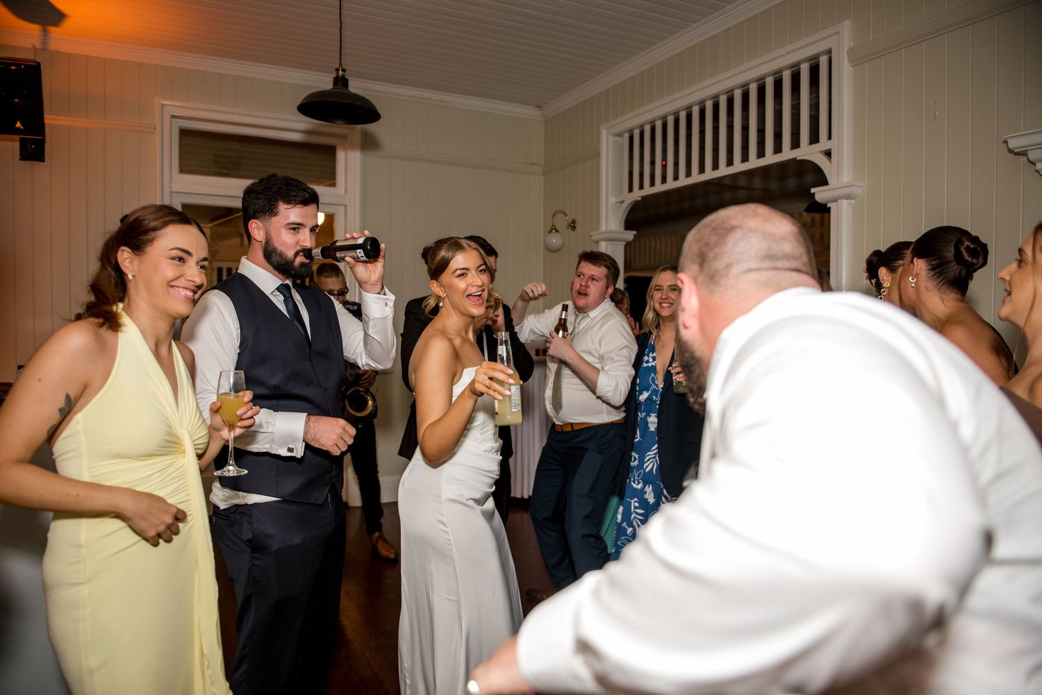Bride in white gown laughing and celebrating with guests holding champagne on the wedding reception dance floor.