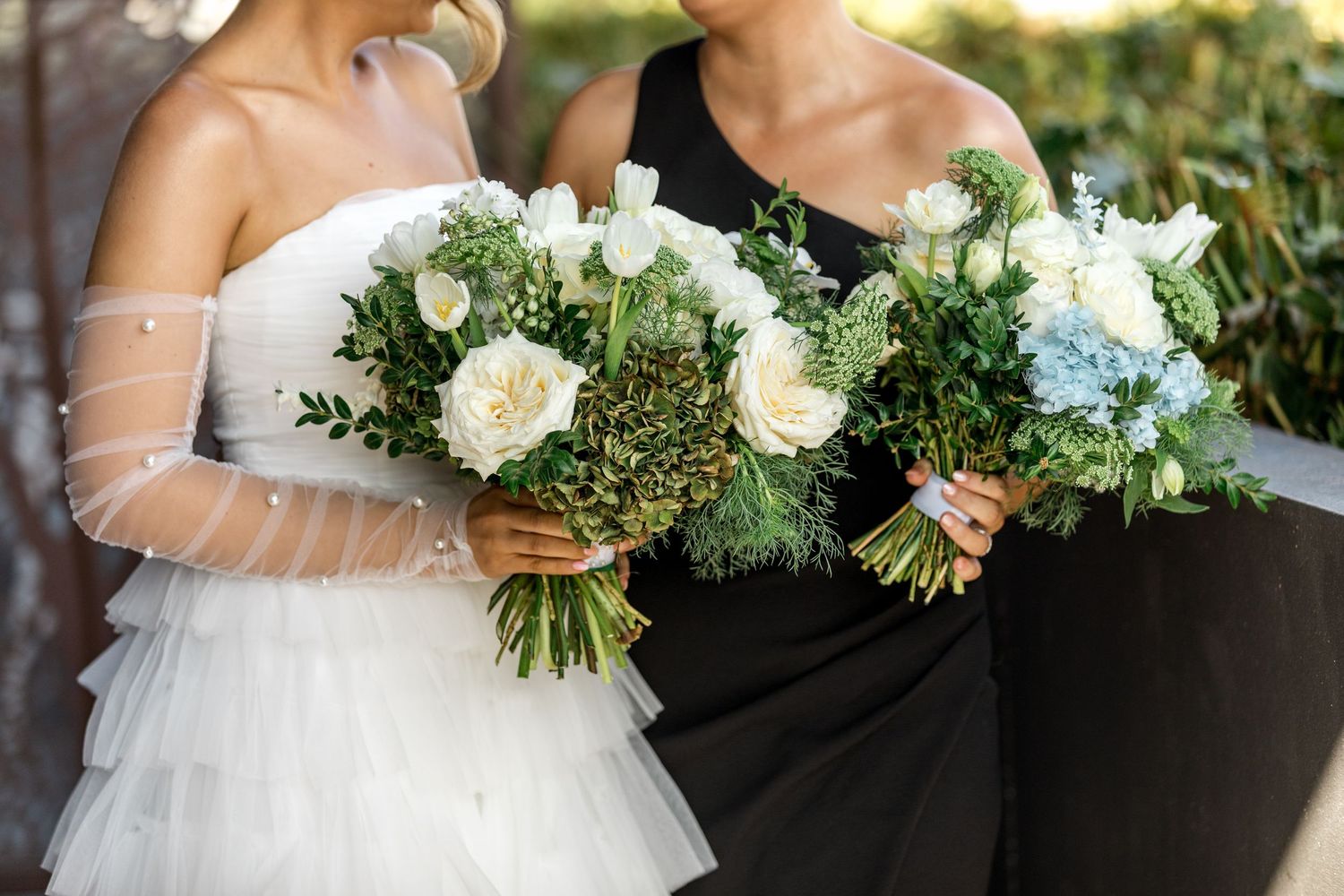 Close-up of bride and bridesmaid holding matching white rose and greenery wedding bouquets.