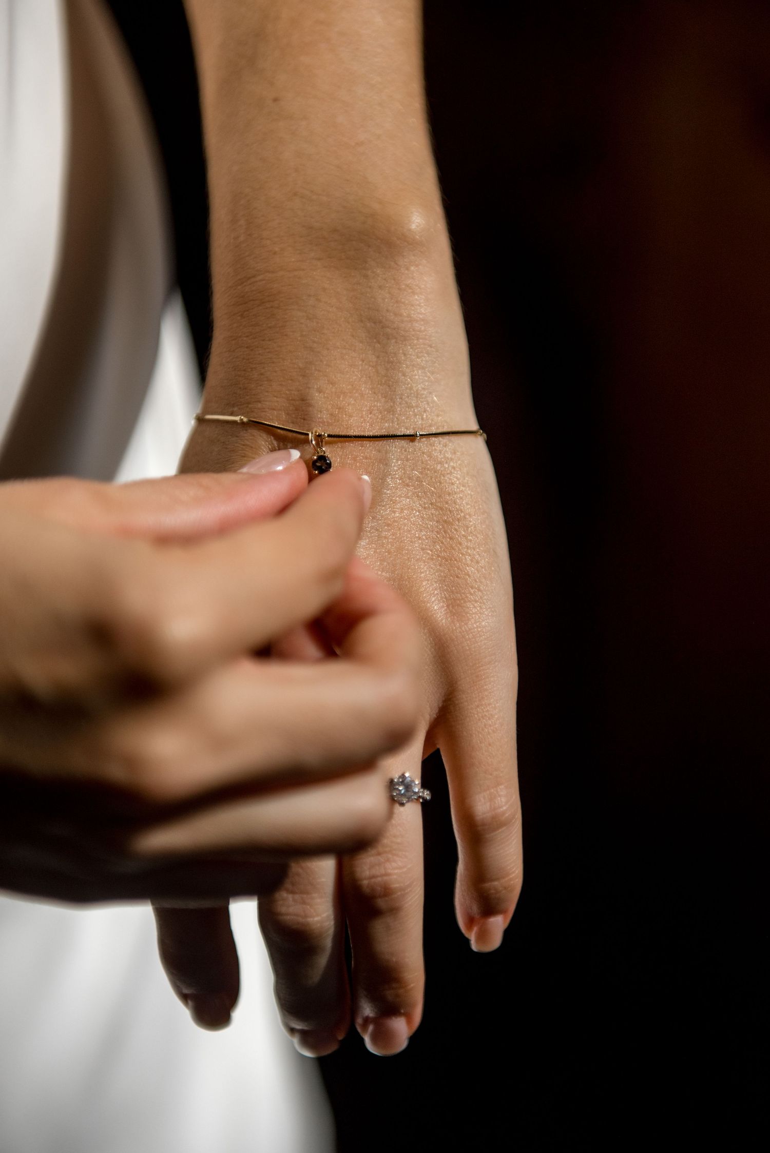 Close-up of a bride's hand wearing a diamond engagement ring and delicate gold bracelet on her wedding day.