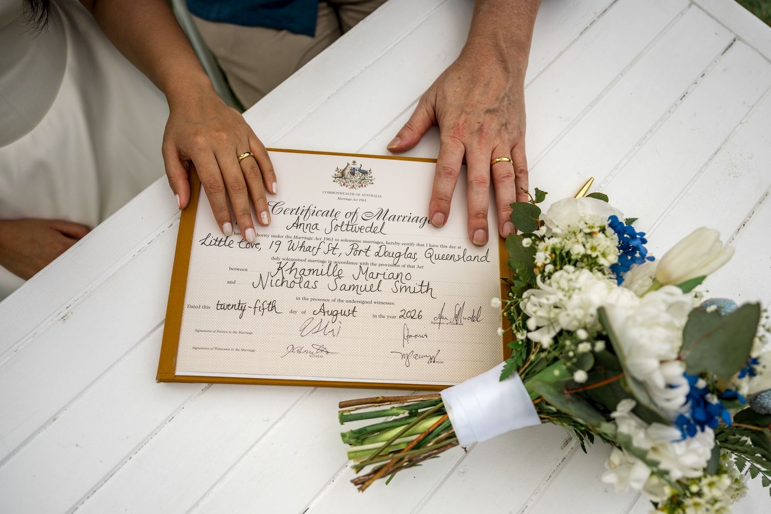 Newlyweds hands resting on a marriage certificate beside a white floral bridal bouquet at Little Cove, Port Douglas.