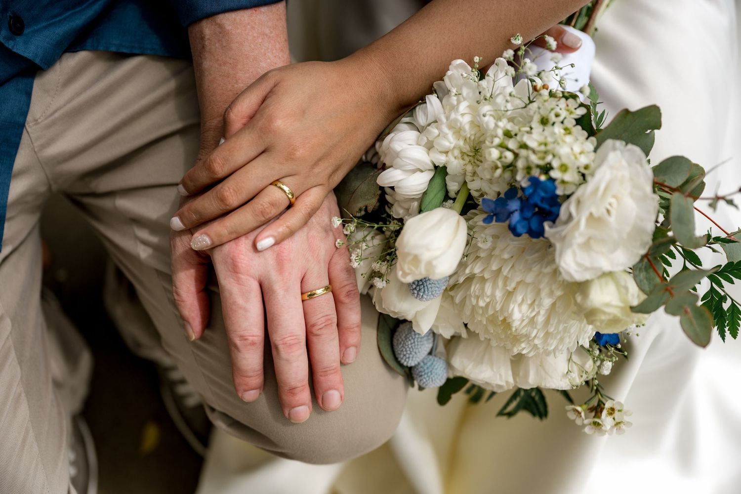 Close-up of newlyweds hands with gold wedding rings resting on a white floral bouquet at Little Cove, Port Douglas.
