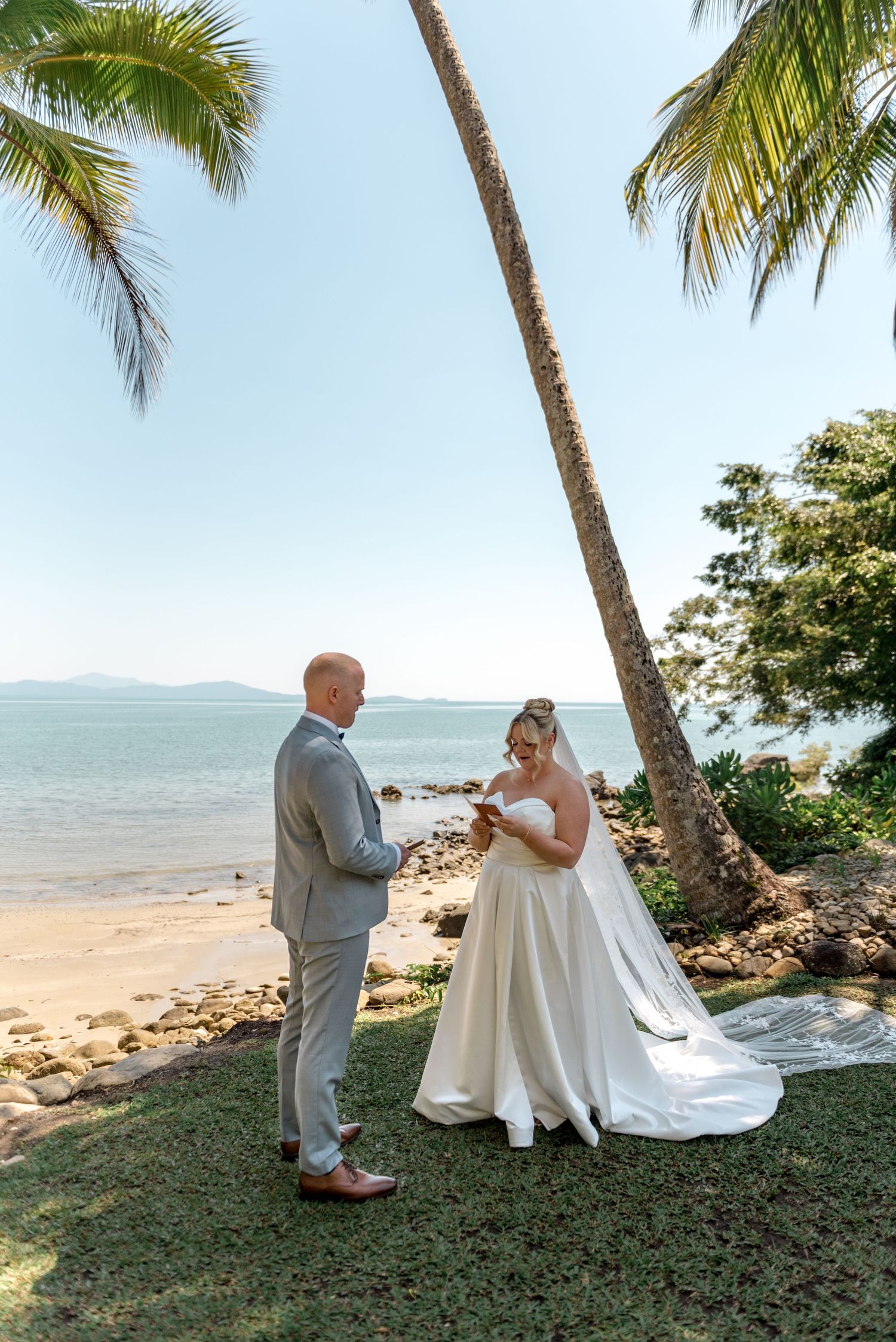 Couple exchanges vows at intimate beach wedding ceremony surrounded by palm trees and ocean views.