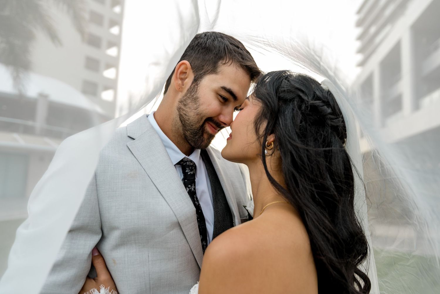 Bride and groom share an intimate nose-to-nose moment under a sheer veil in soft misty light.