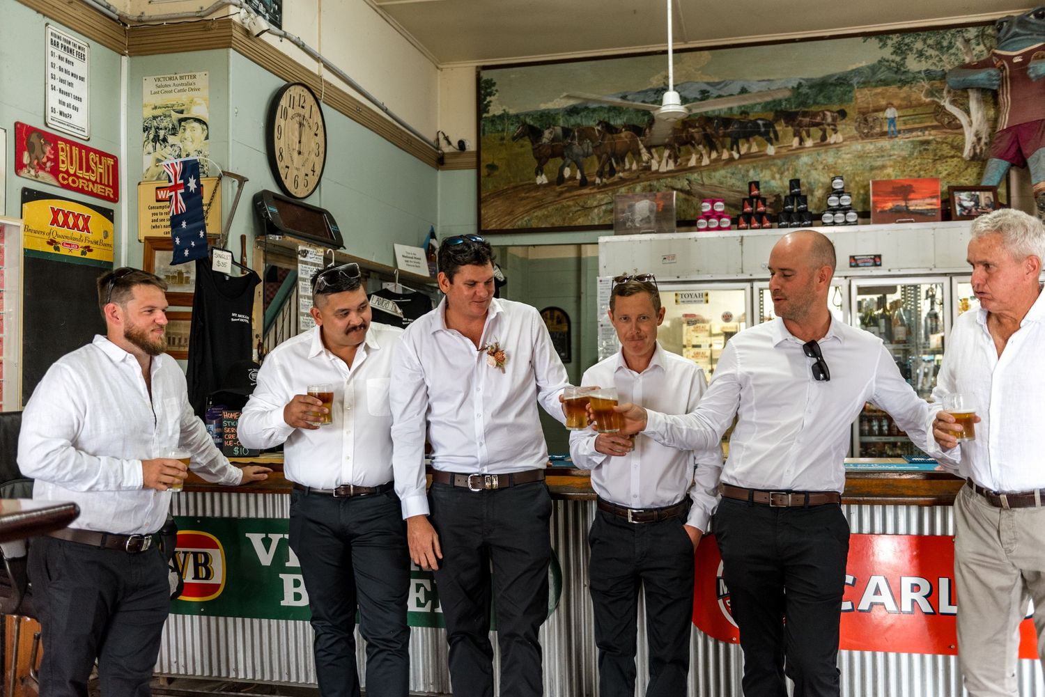 Groomsmen in white shirts sharing drinks and laughing together at a rustic bar before the wedding.