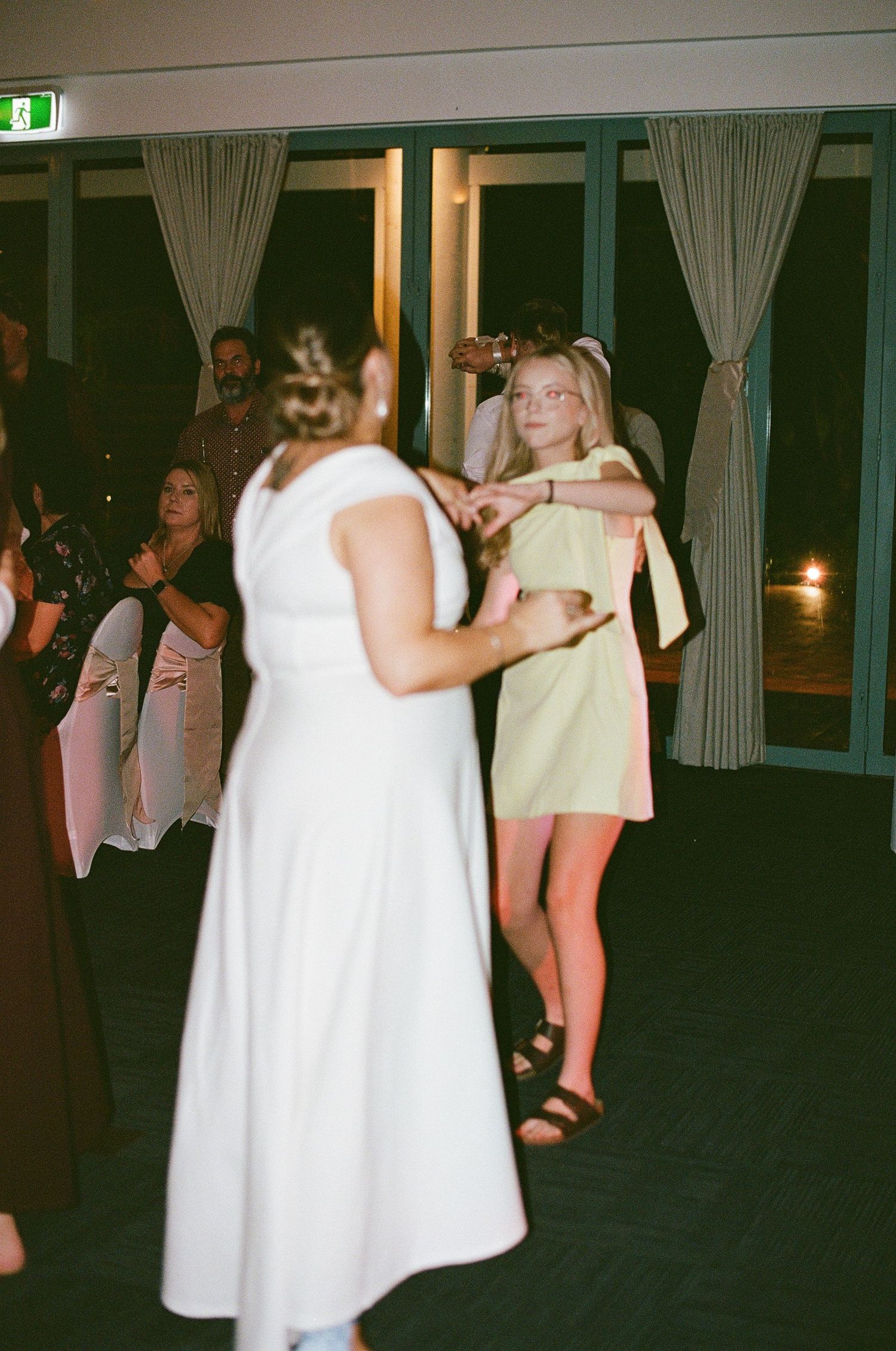 Young woman in green dress dancing at a wedding reception venue.