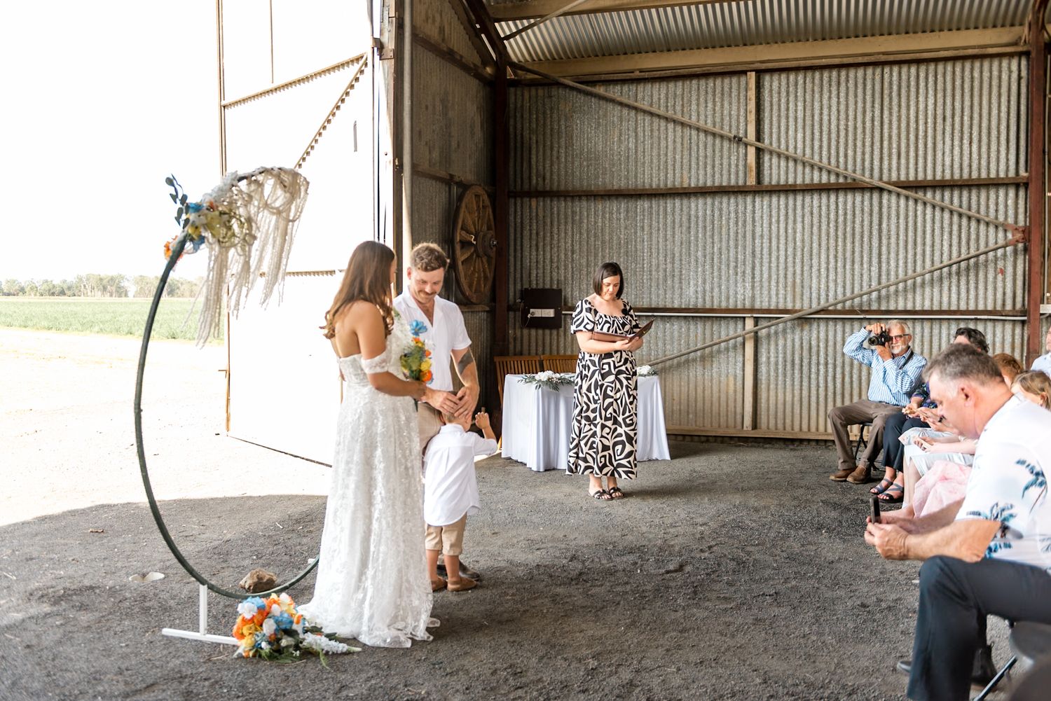 Bride and groom exchange vows under circular macrame arch in rustic barn wedding ceremony.