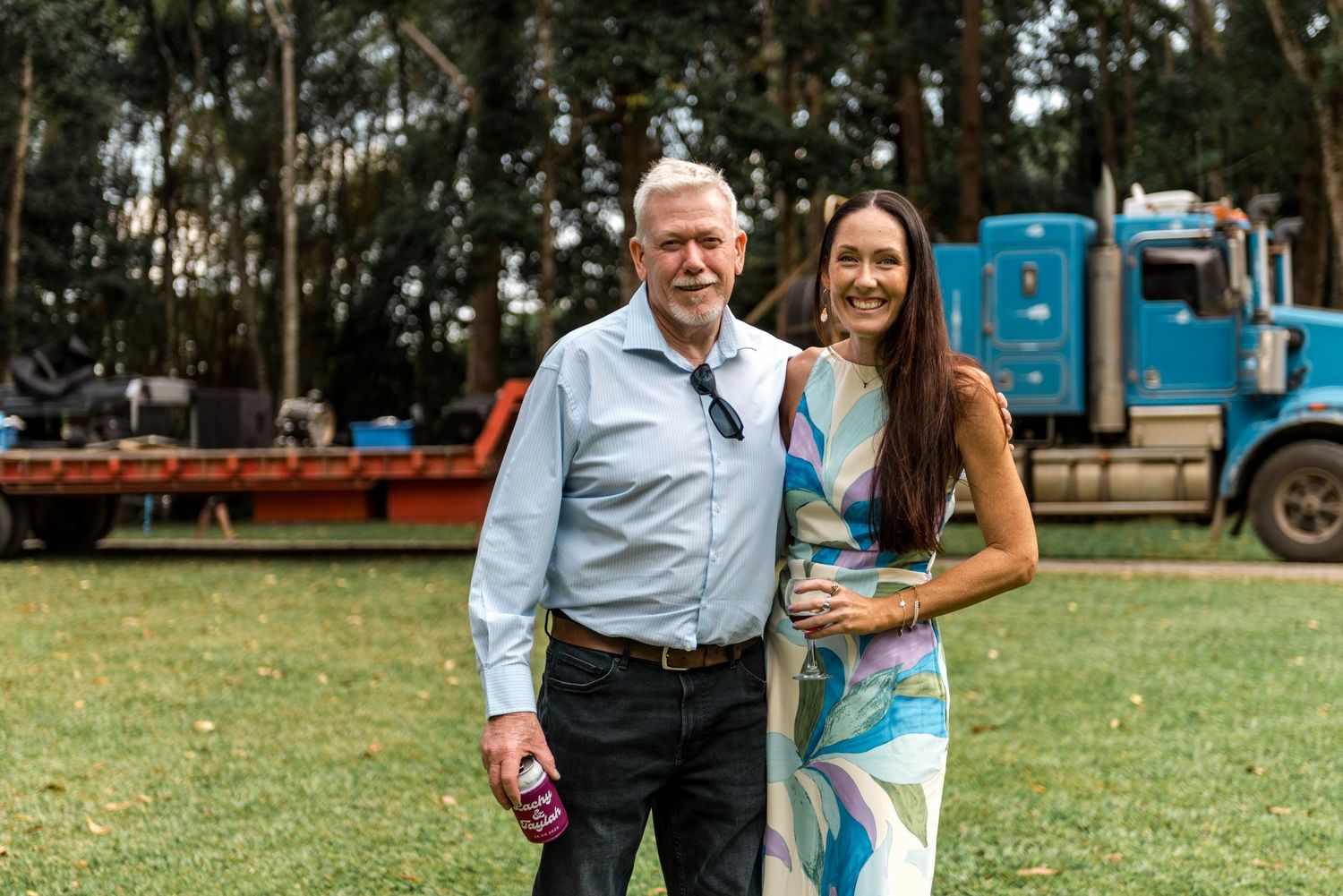Older man and young woman smiling together outdoors at casual event with blue truck in background.