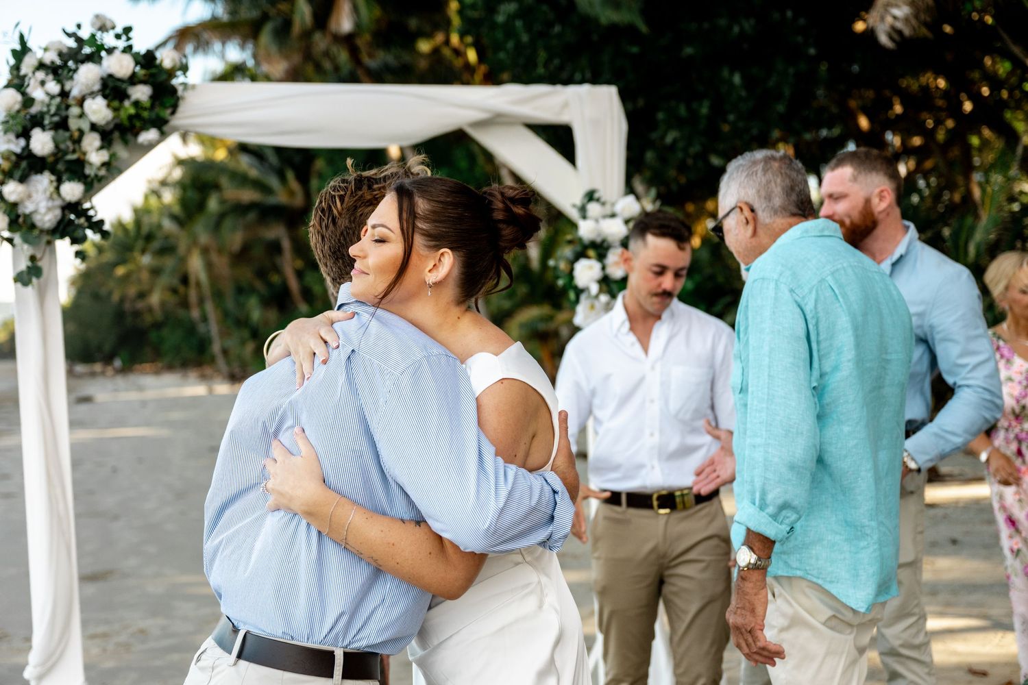 Bride hugging a guest in a blue shirt after a tropical beach wedding ceremony at Four Mile Beach, Port Douglas.