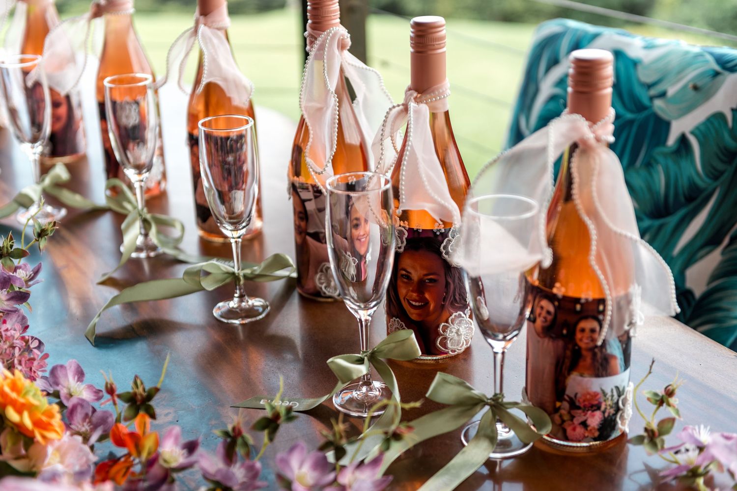 Personalized wine bottles with photo labels and champagne flutes arranged with colorful floral centerpieces.
