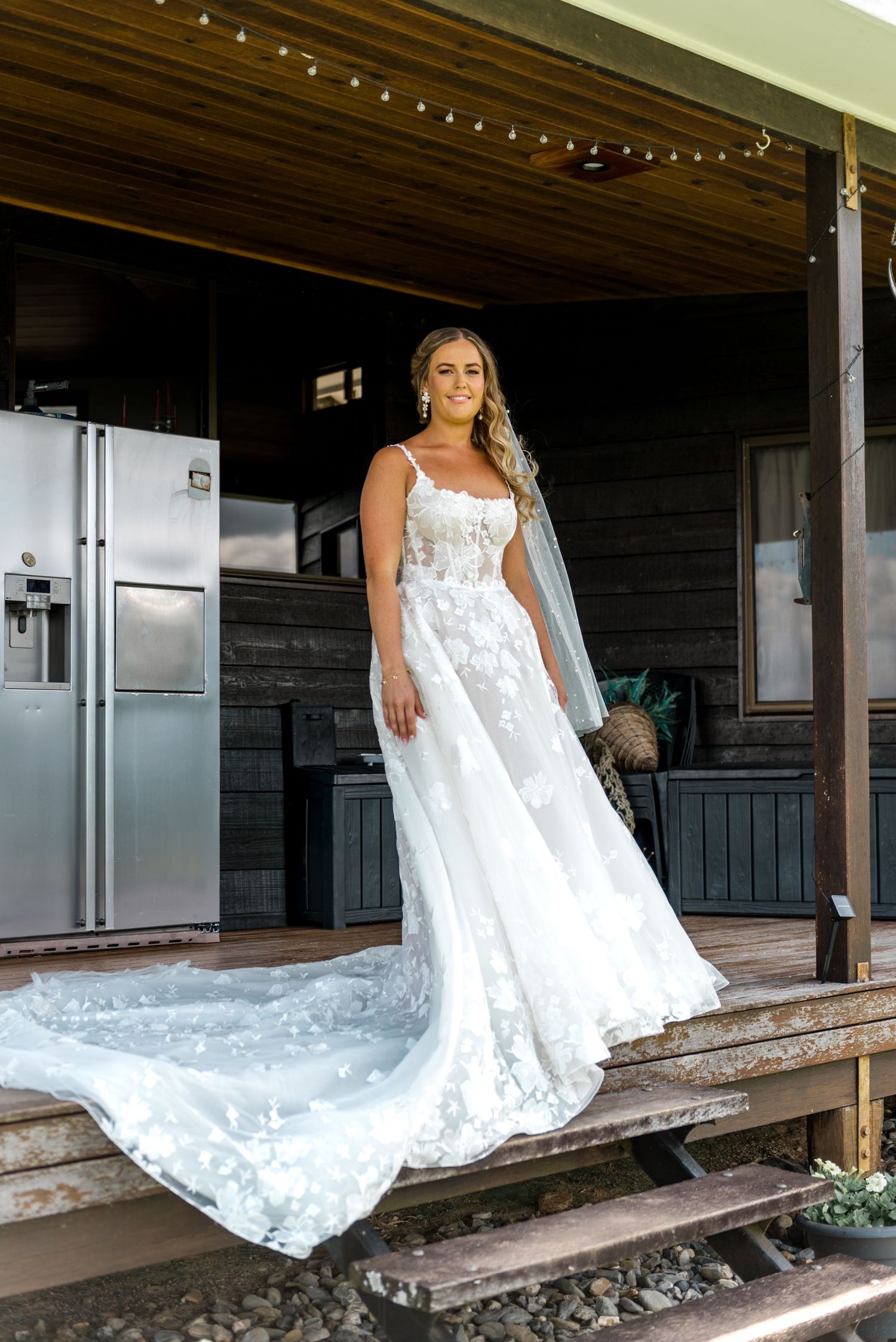 Bride in elegant lace A-line wedding gown with cathedral train poses on rustic wooden steps.