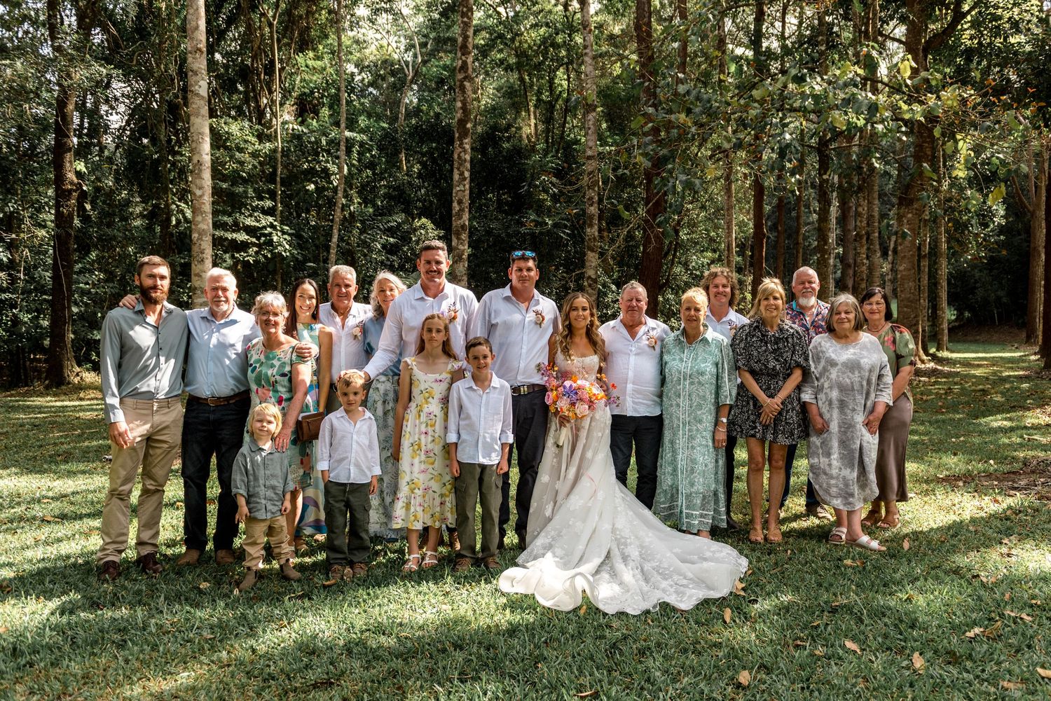 Large family group portrait with bride and groom at outdoor woodland wedding celebration.