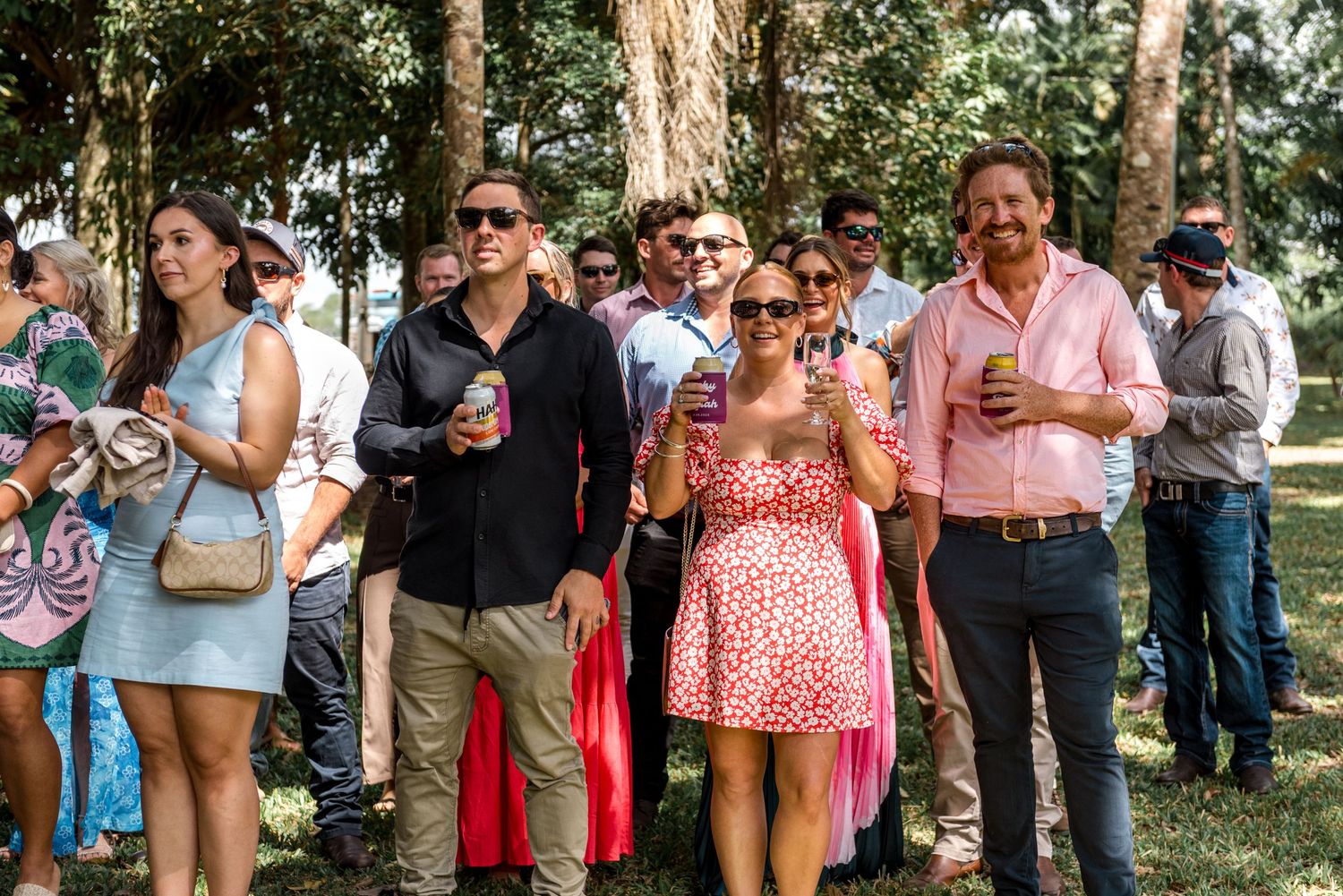 Guests mingle outdoors at a wedding ceremony in a lush green park setting.