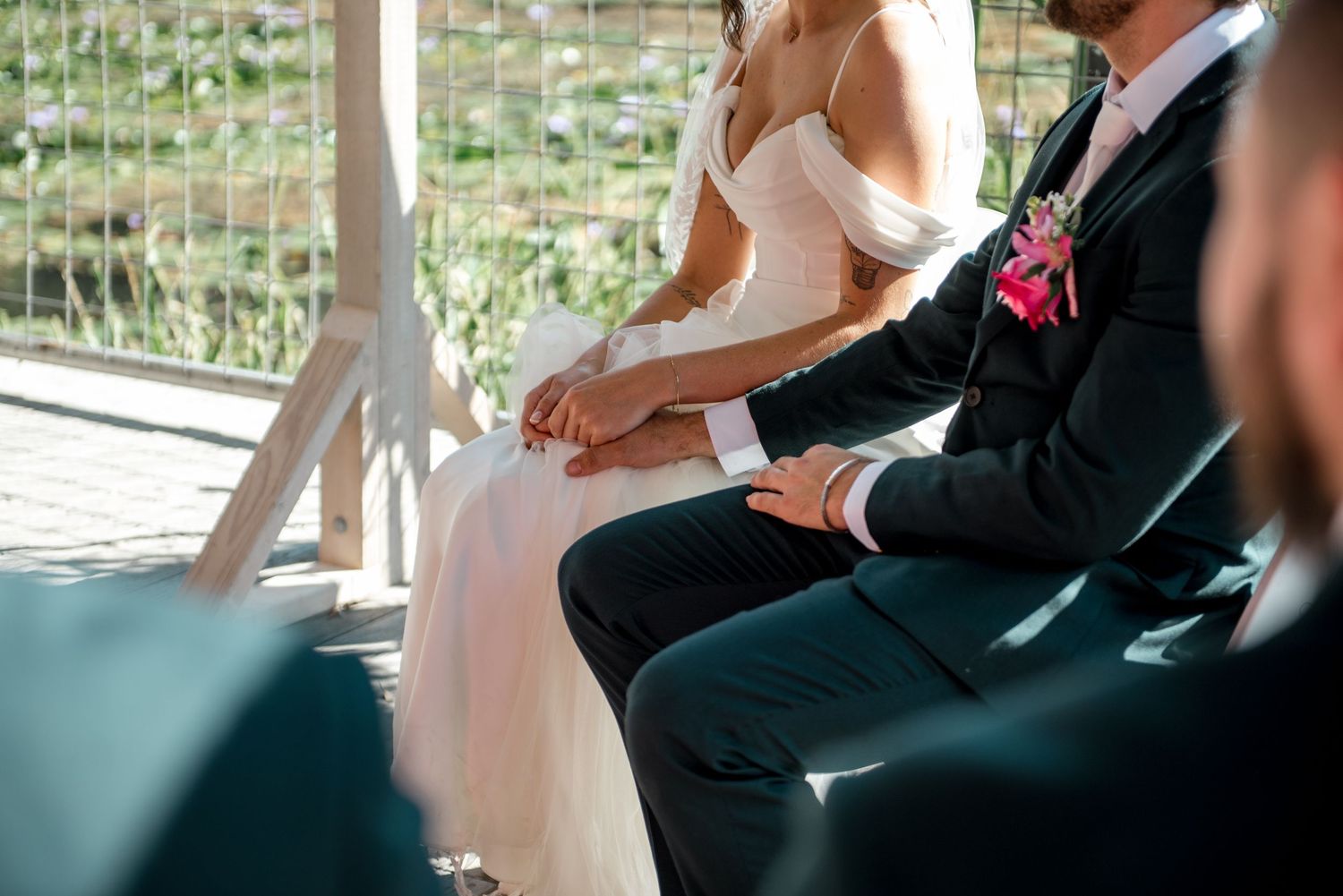 Bride in white gown and groom in dark suit hold hands during outdoor wedding ceremony.