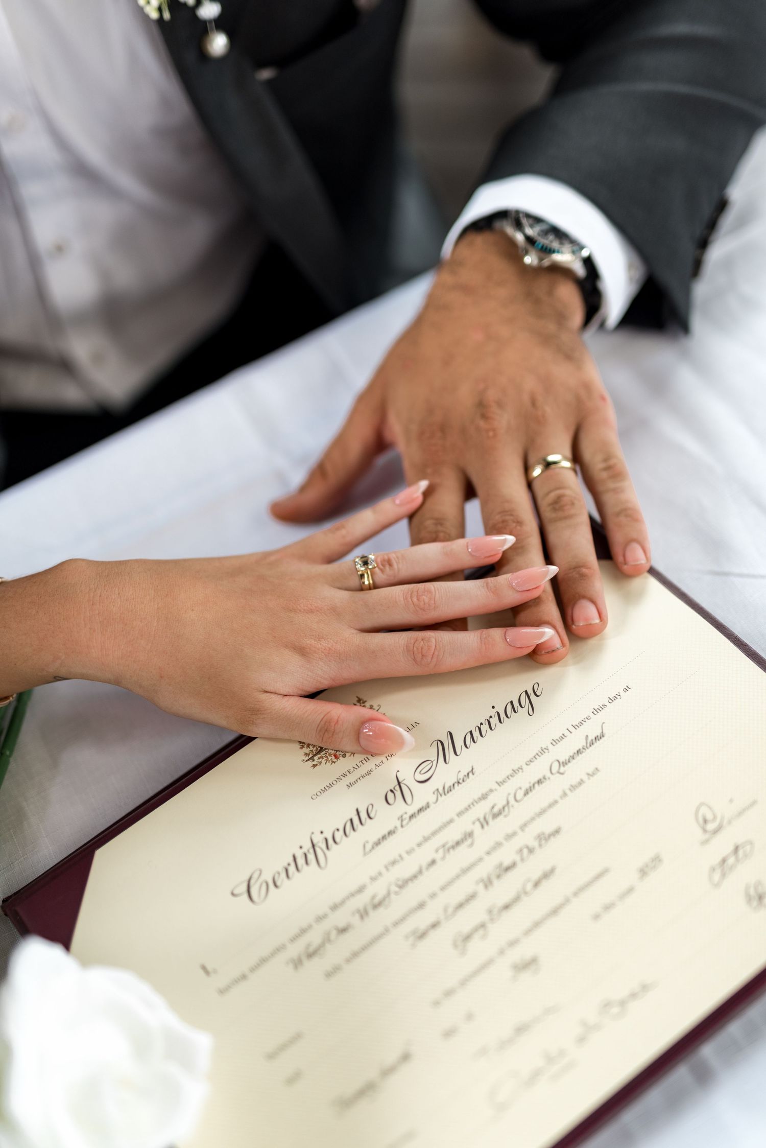 Newlyweds placing hands on marriage certificate showing wedding rings after ceremony.