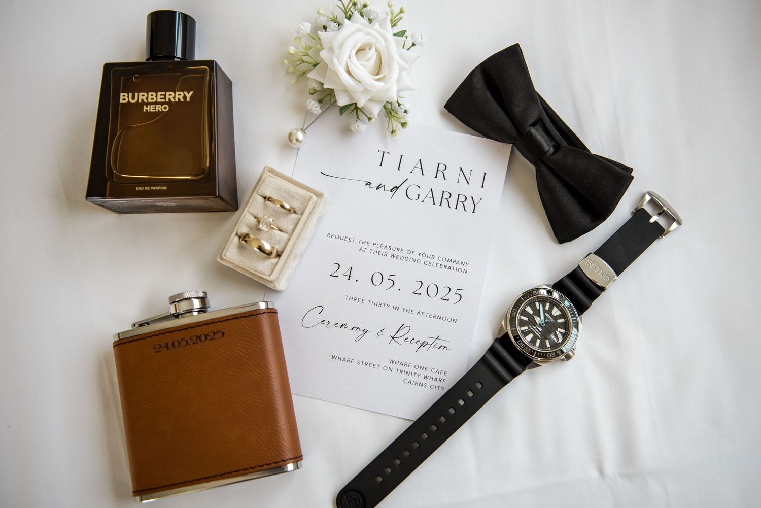 Groom wedding flatlay with Burberry cologne, watch, bow tie, flask, and invitation.