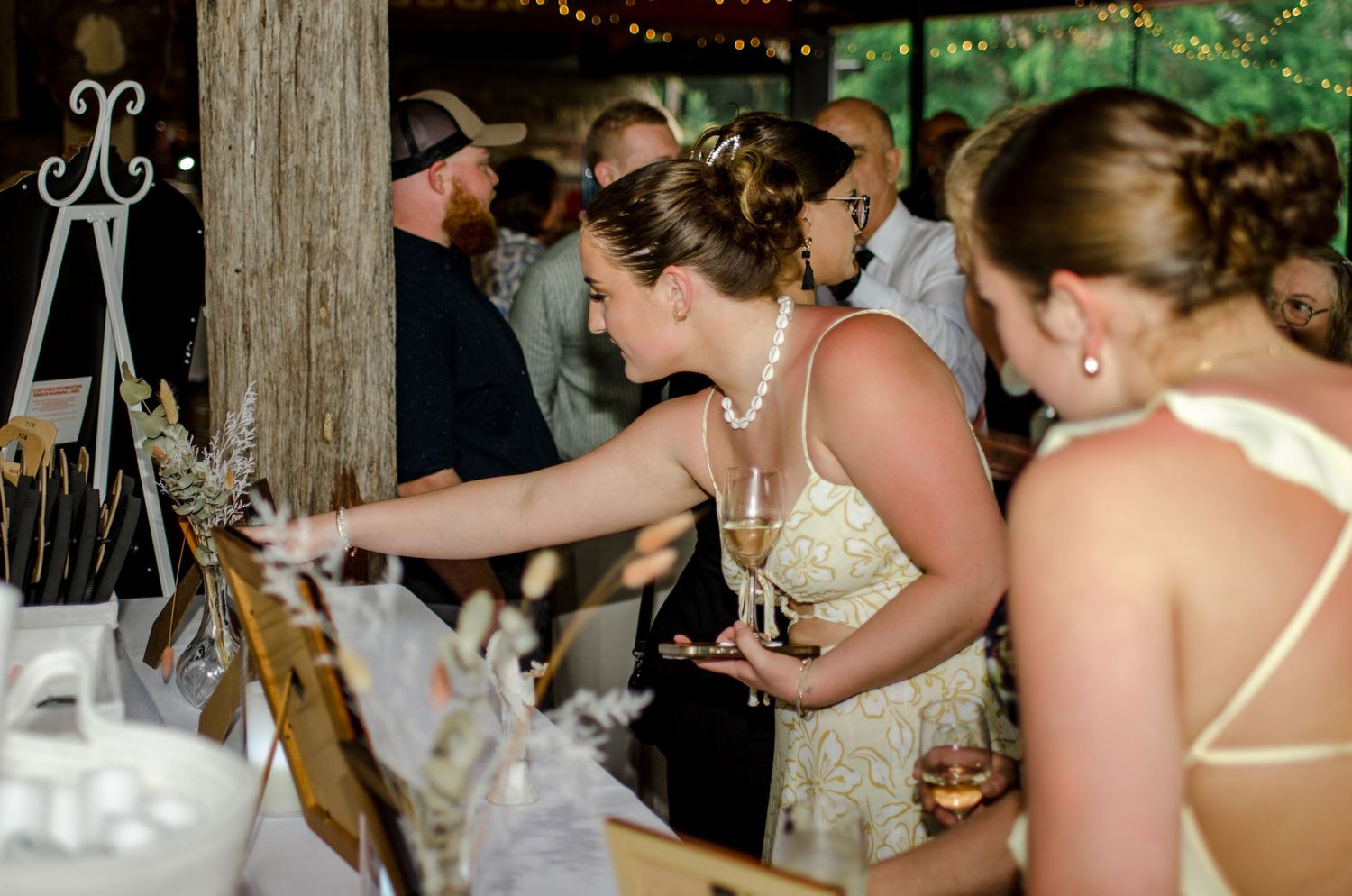 Bride in lace gown reaches toward a decorative display at an elegant rustic indoor wedding reception.