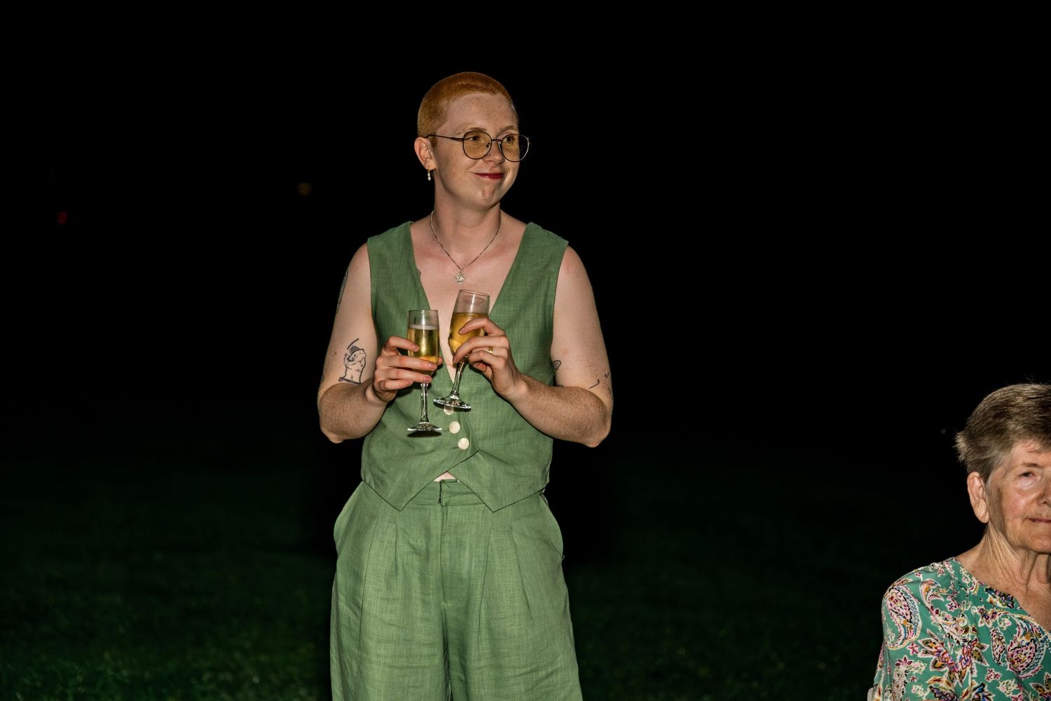 Person in green linen outfit holding a champagne glass during an outdoor evening celebration.