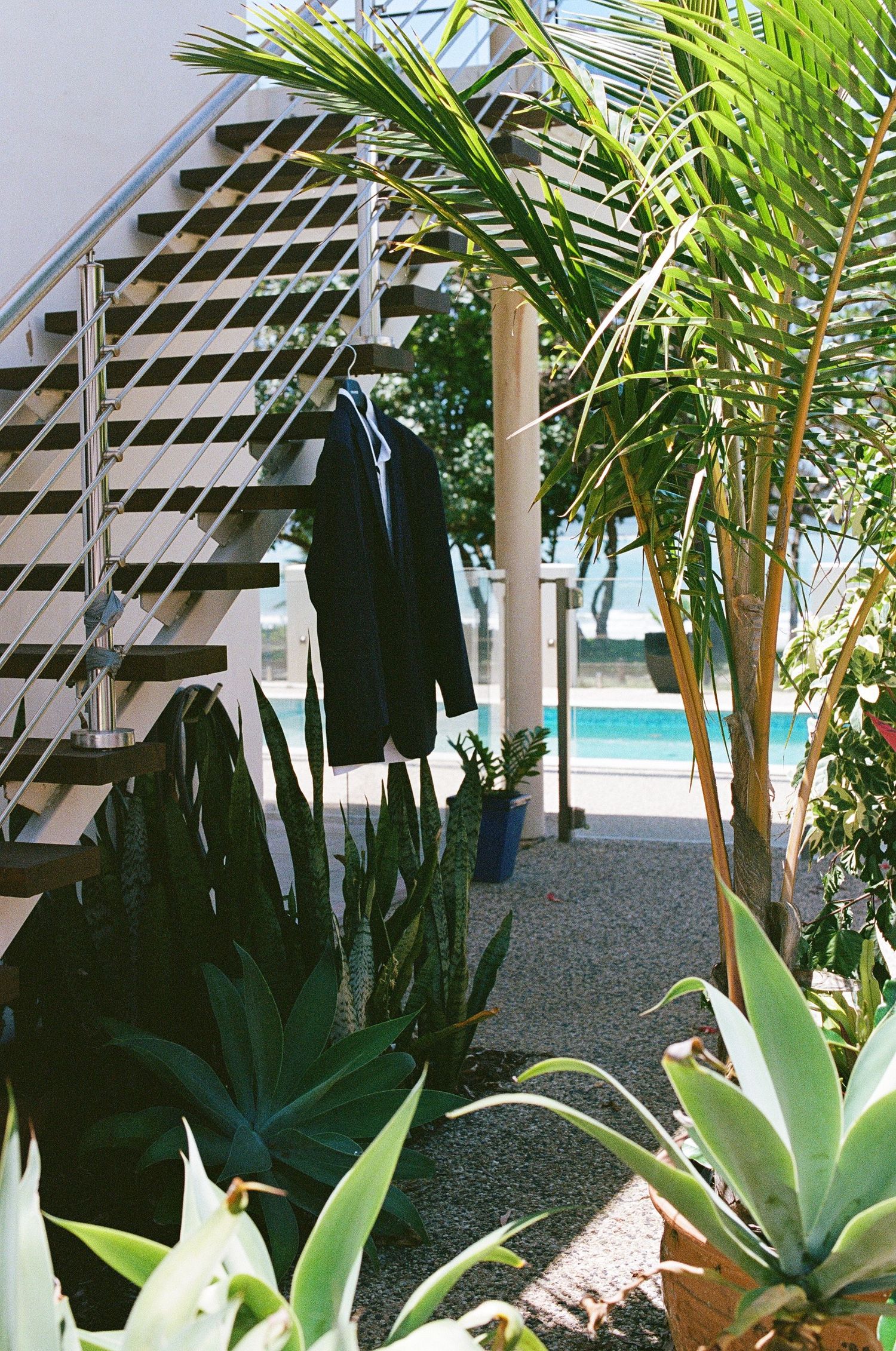 Black suit jacket hanging on staircase railing beside tropical plants near a pool.