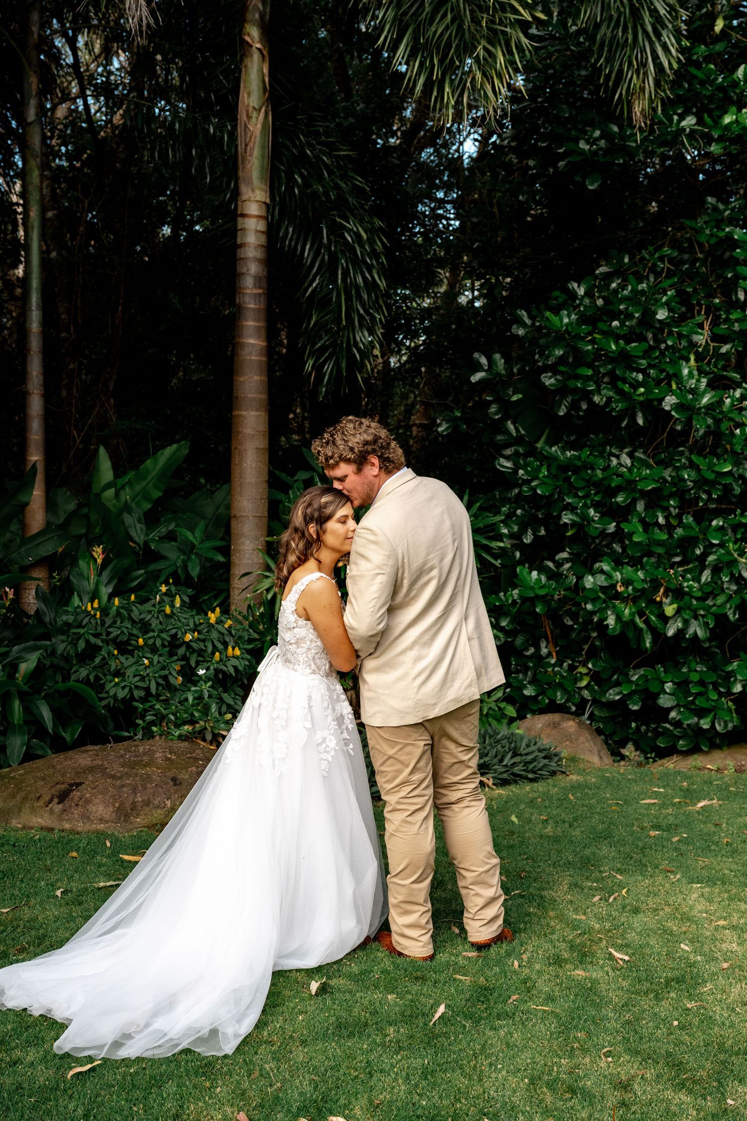 Bride and groom embracing tenderly in a lush tropical garden setting.