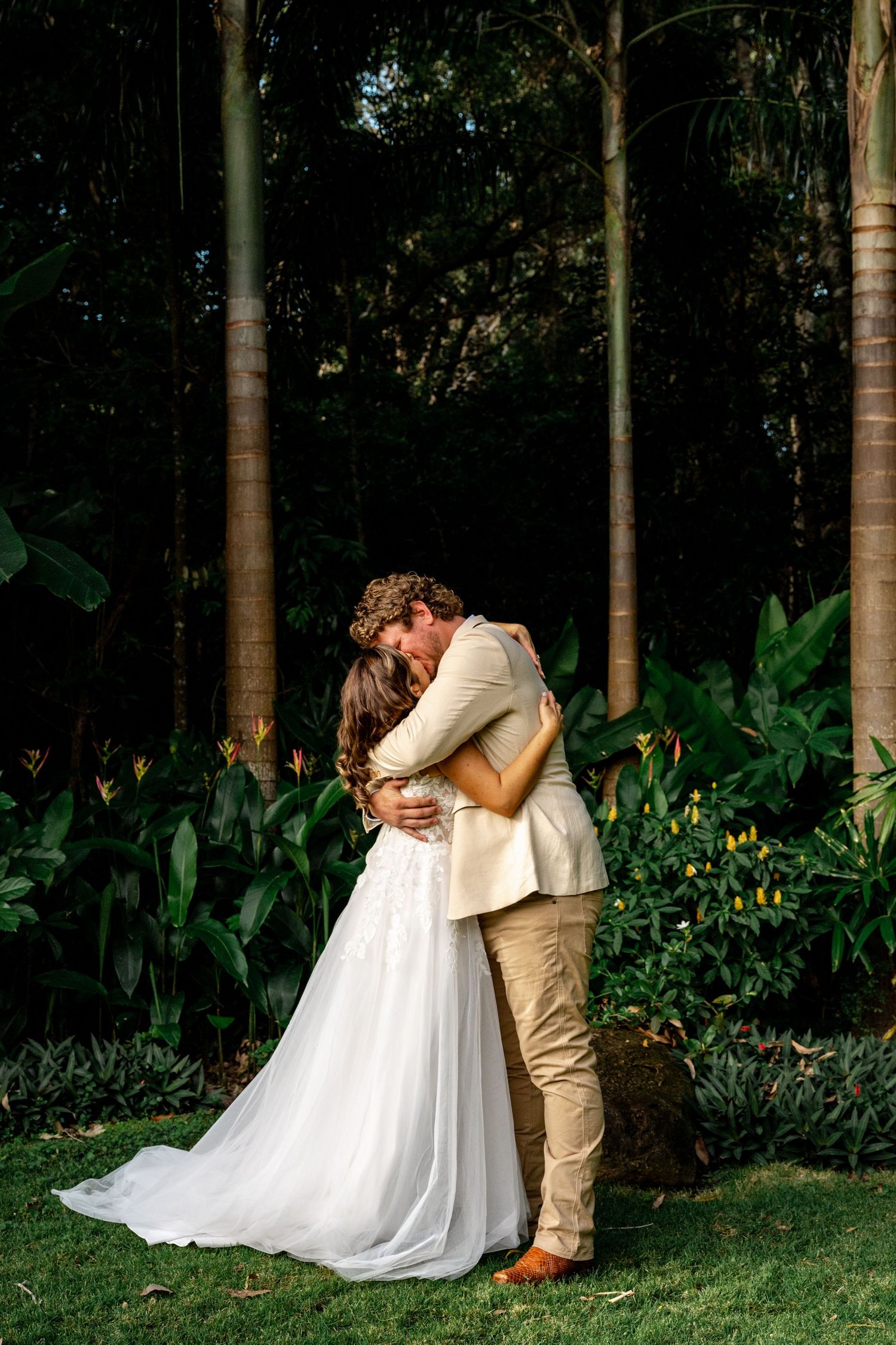 Newlywed couple shares romantic embrace surrounded by tropical palms and lush greenery after ceremony.