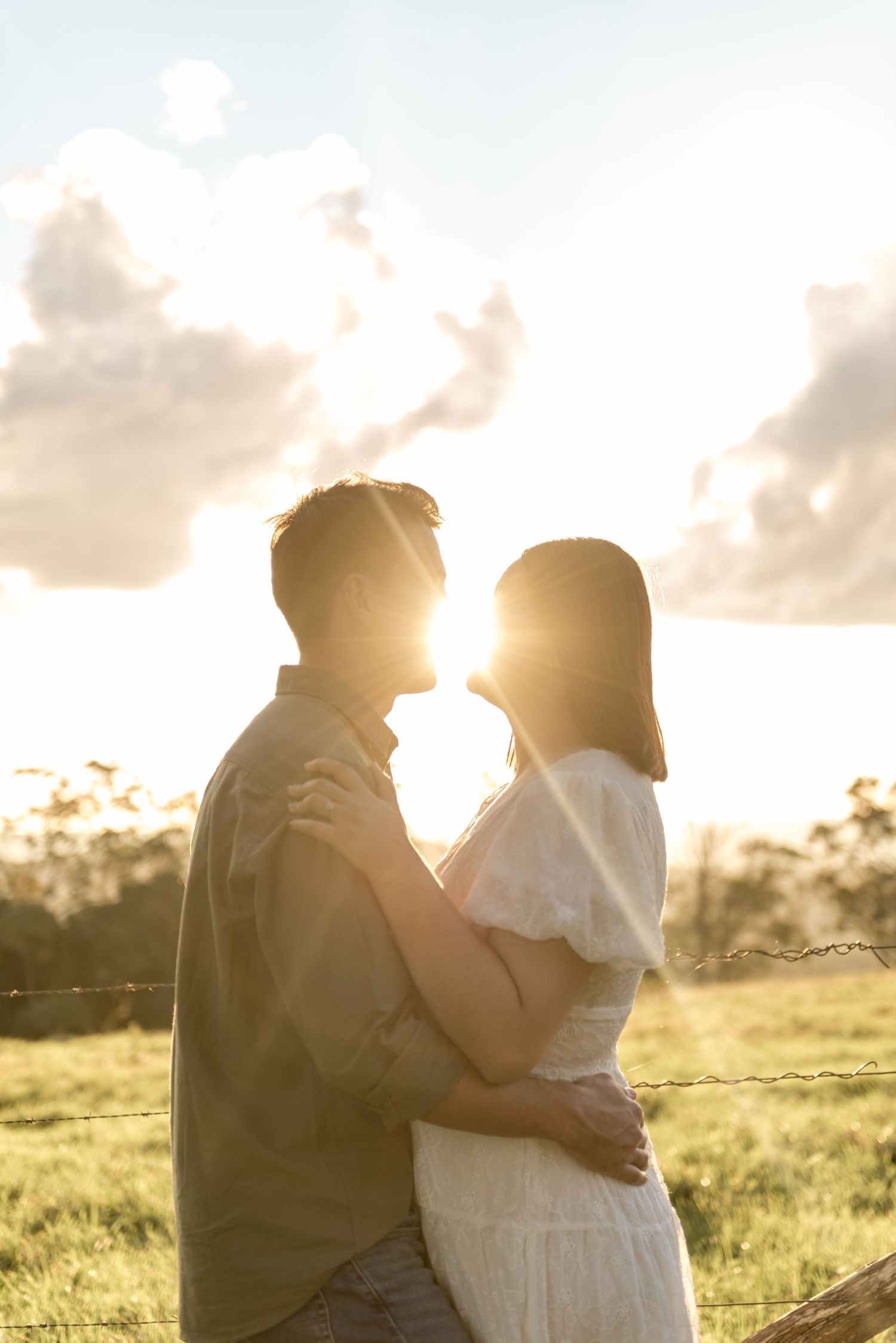 Couple holding each other in a sun-drenched field with golden hour backlight.