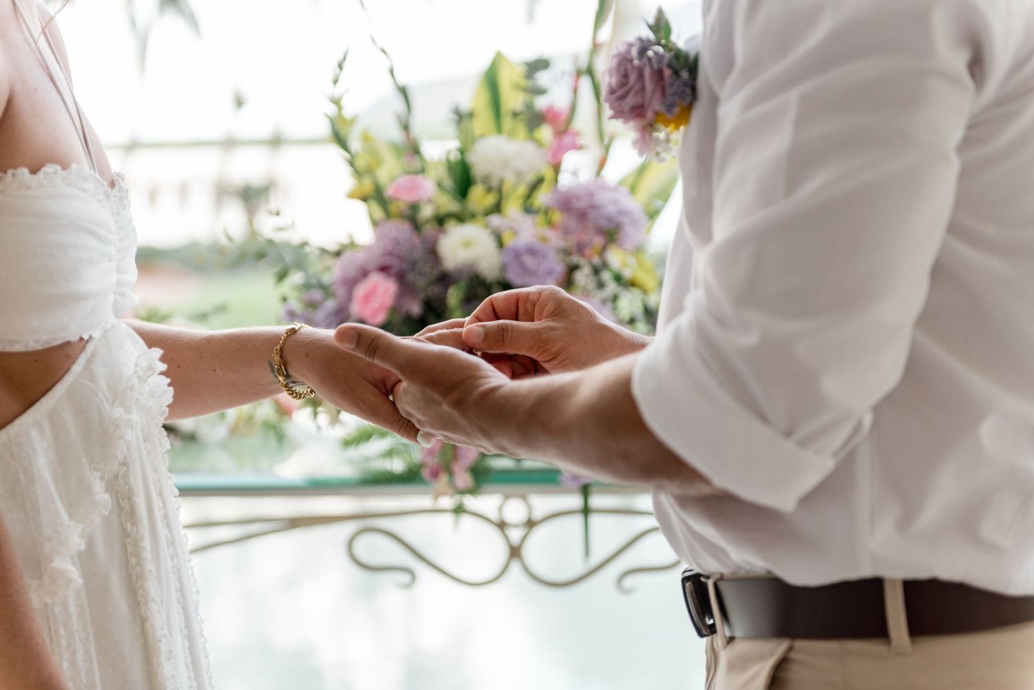 Close-up of groom placing wedding ring on bride's wrist during tropical wedding ceremony.