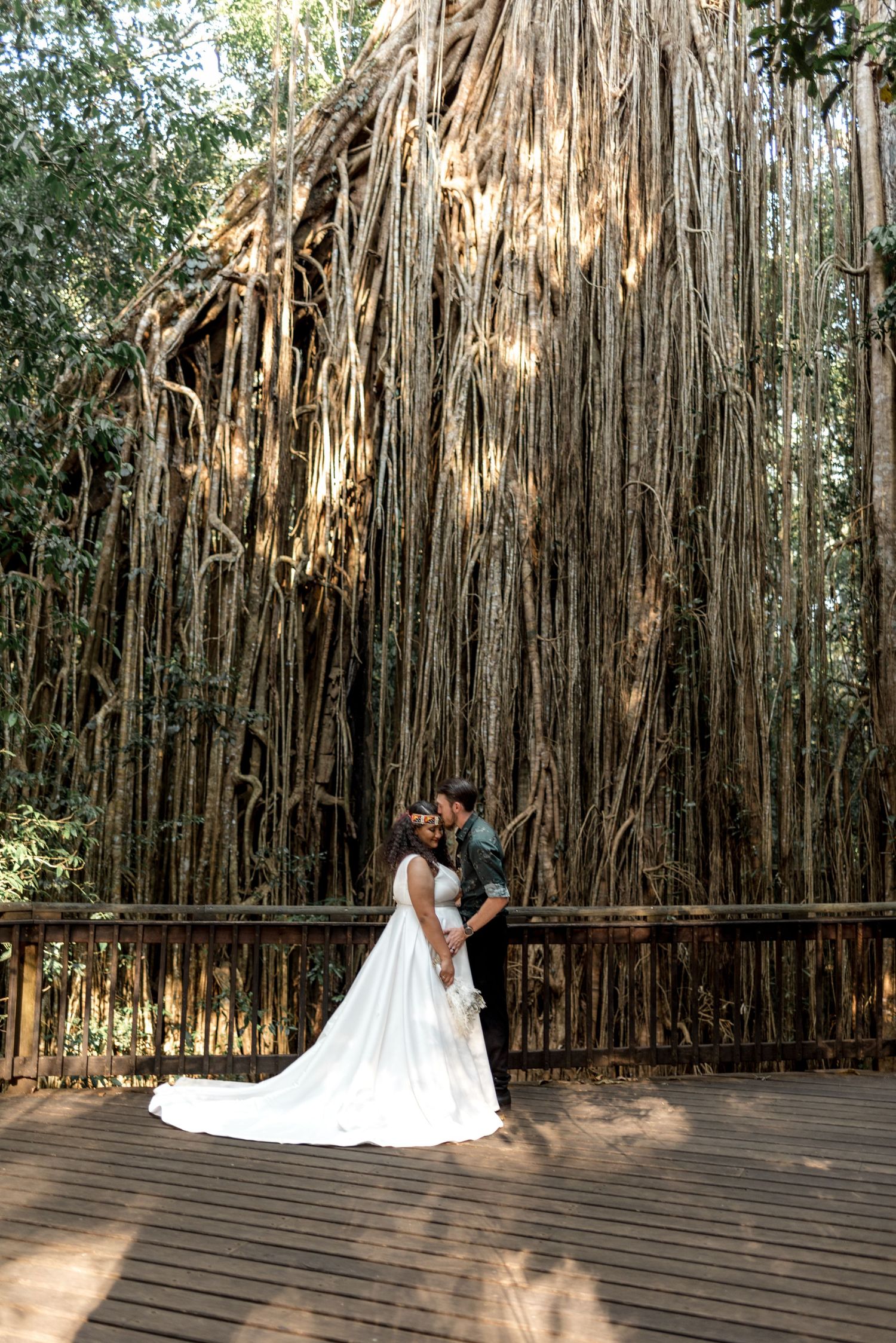 Wedding couple embracing on a wooden deck surrounded by dramatic hanging banyan tree roots.