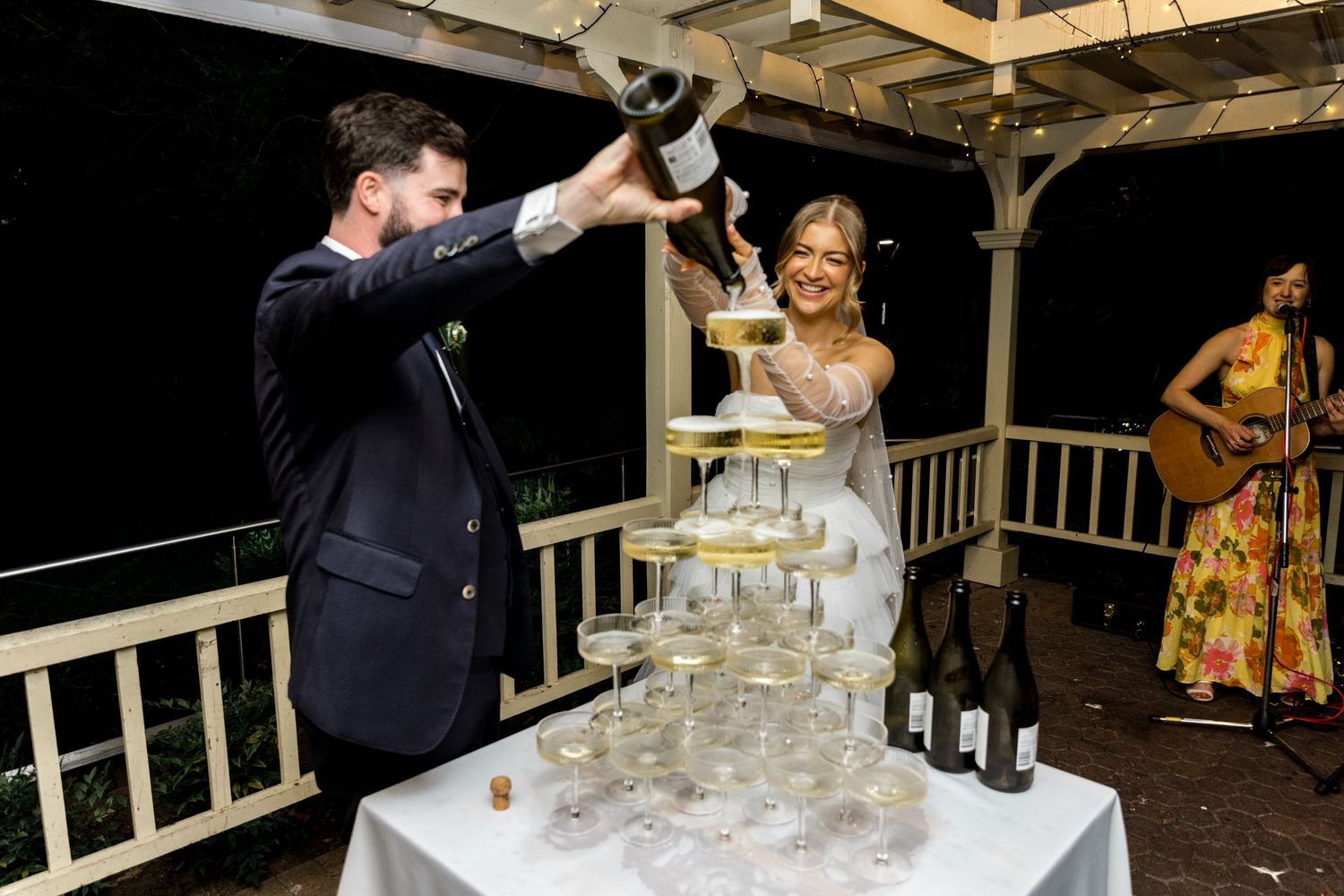 Bride and groom pour champagne together into a tall glass tower at wedding.
