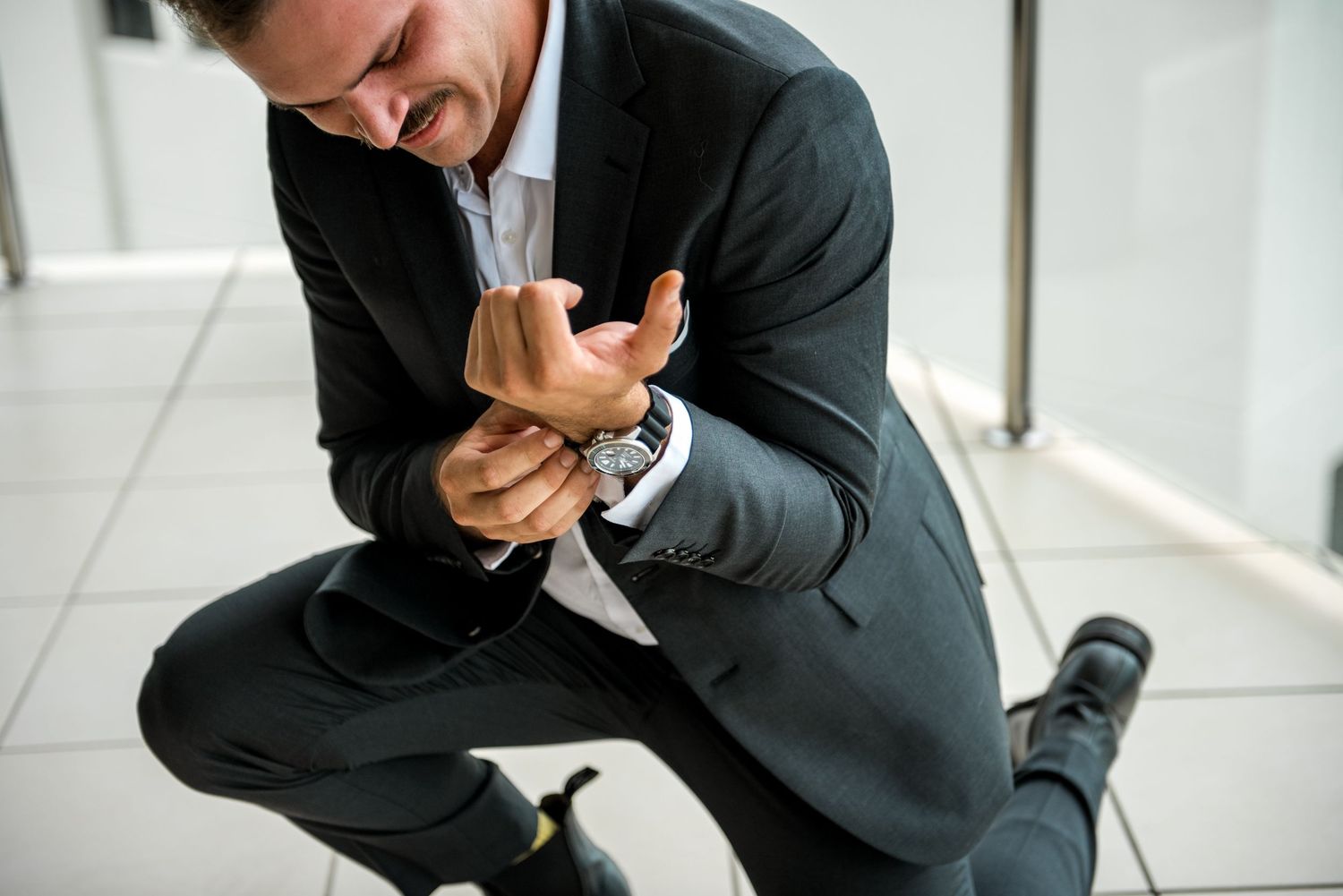 Groom in dark suit kneeling while adjusting his cufflinks before wedding ceremony.