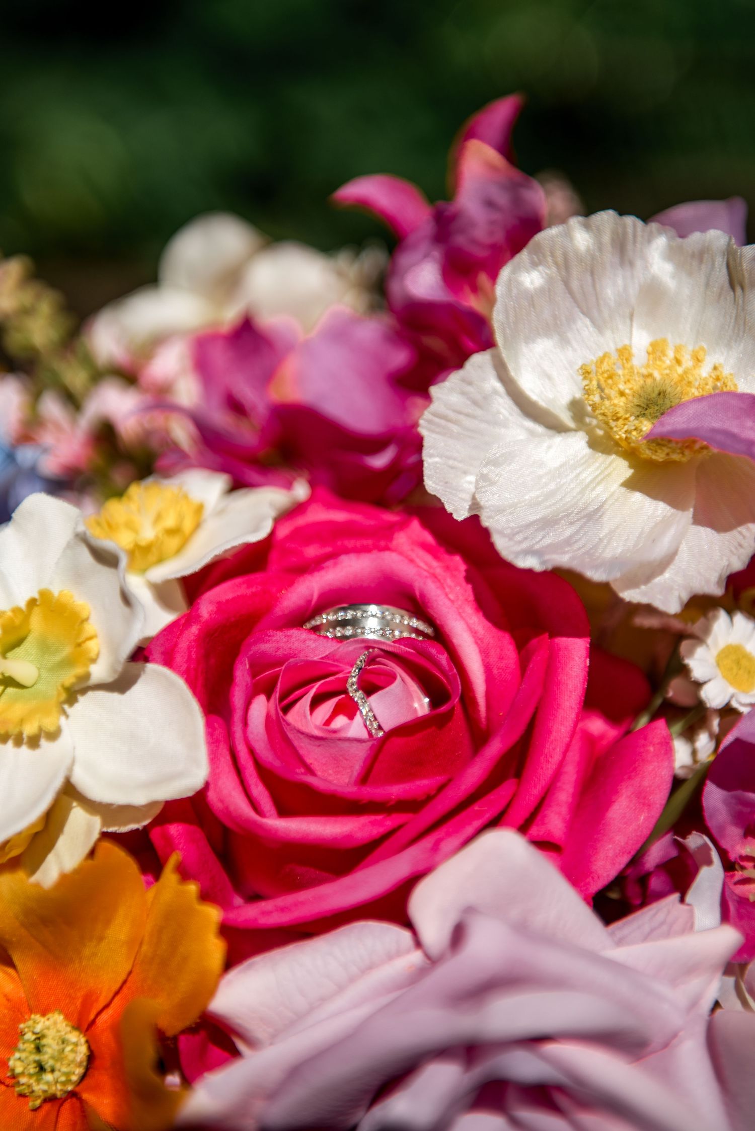 Diamond wedding rings nestled in a vibrant colorful bridal bouquet with roses.