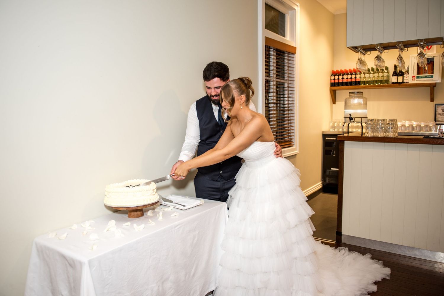 Bride and groom cutting their white wedding cake together at their indoor wedding reception.